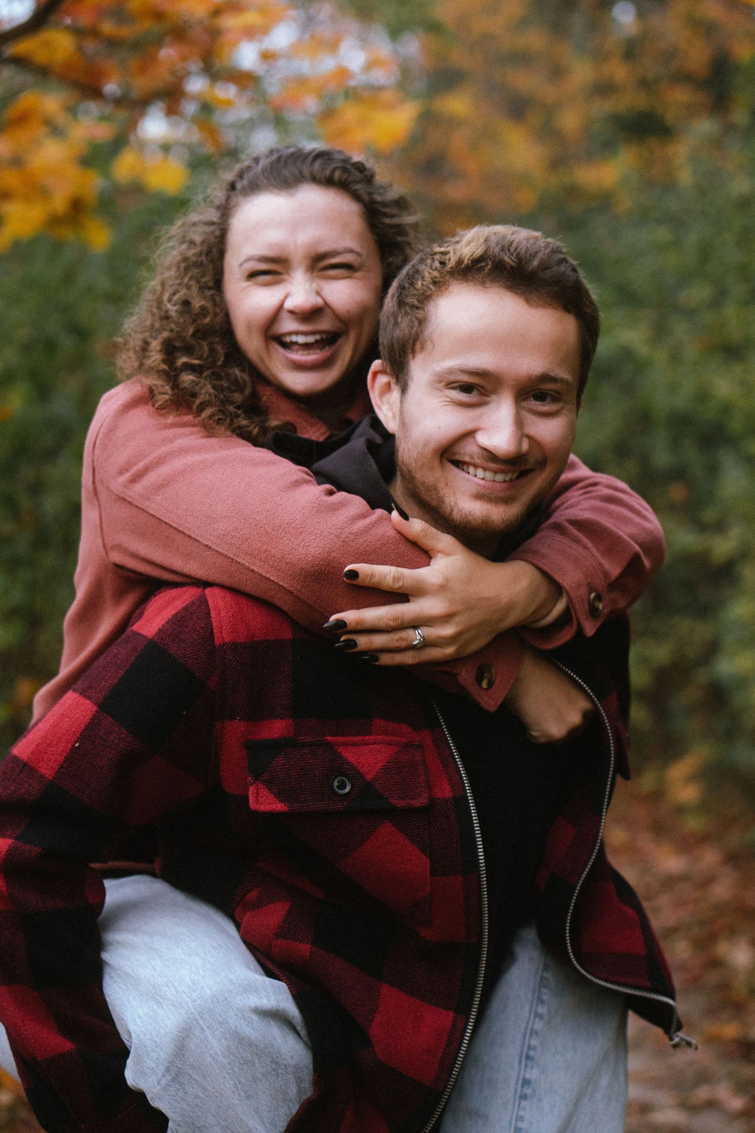 Playful couple in buffalo plaid embracing and laughing during autumn photoshoot.