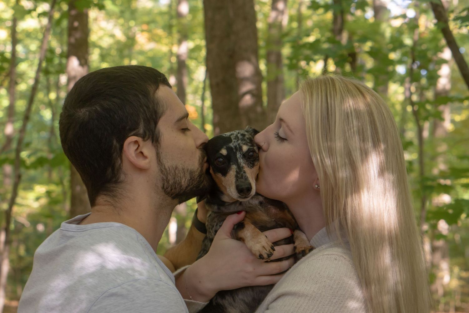 A romantic couple shares a tender kiss in a sunlit forest setting during a photoshoot.