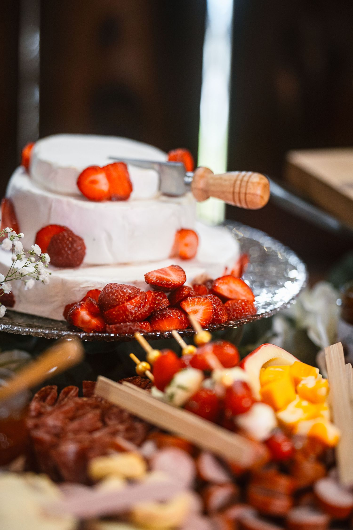A white frosted cake decorated with fresh strawberries next to a charcuterie spread.