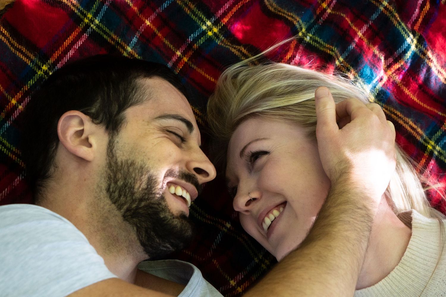 A couple sharing a joyful moment together on a plaid blanket.