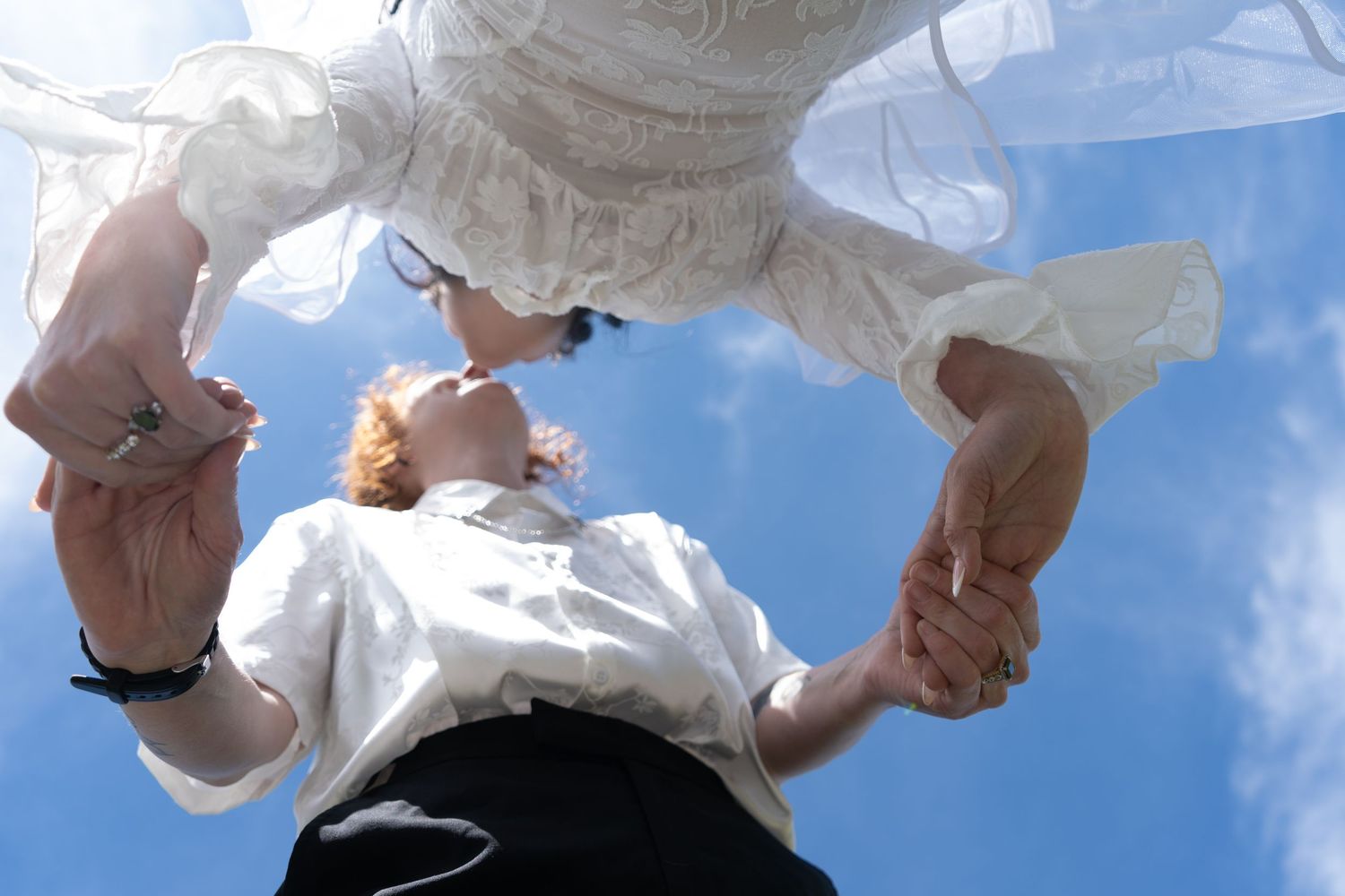 A person's hand holds up a crumpled plastic bag against a bright blue sky with white clouds.