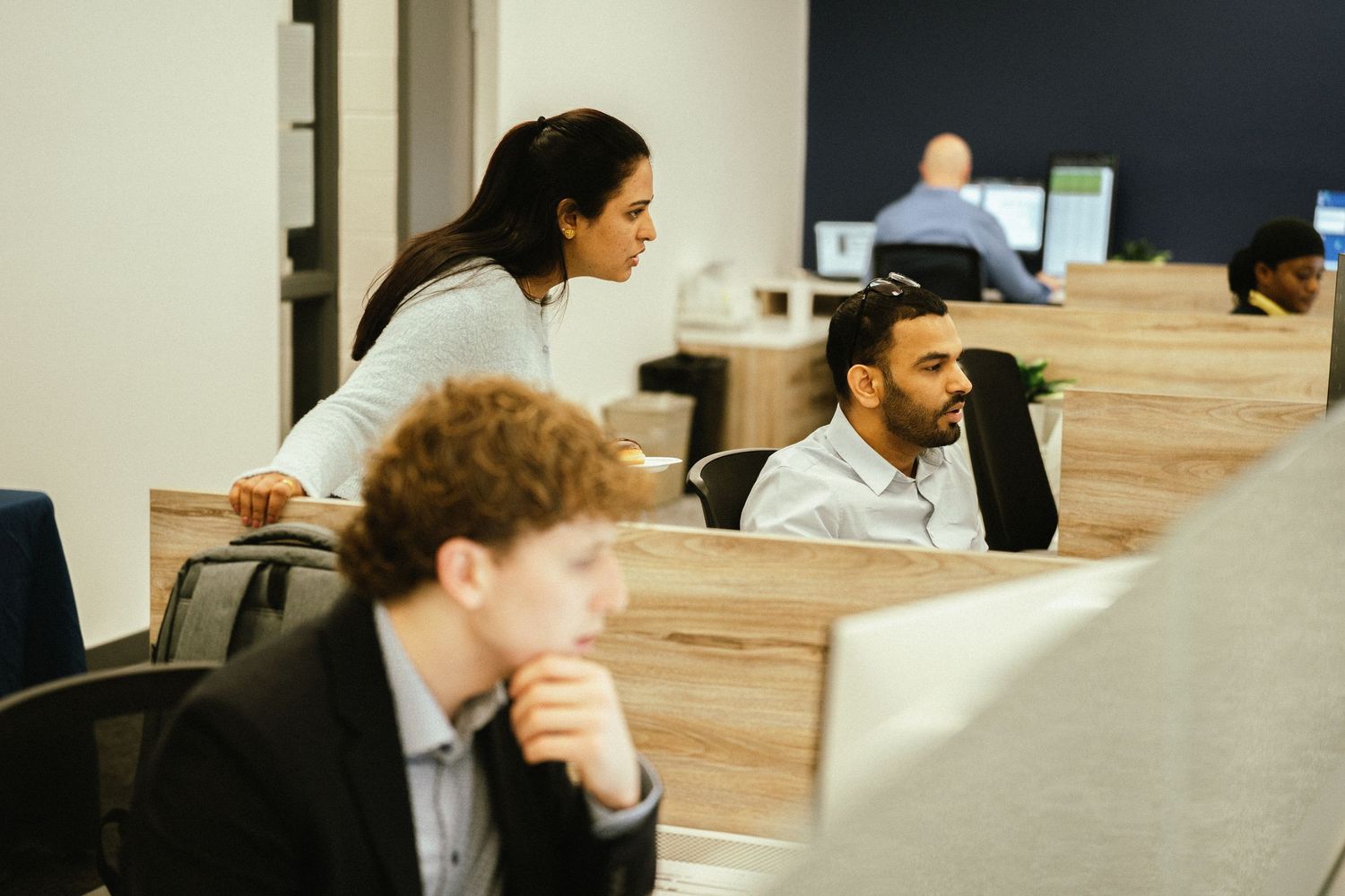 Employees working at their desks in an open office environment with cubicle workstations.