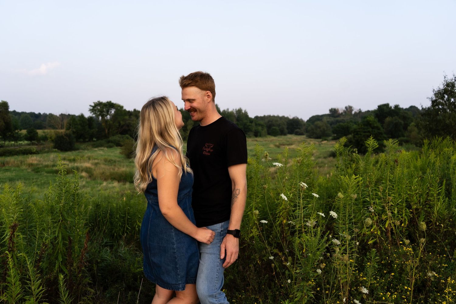 A couple shares a romantic moment together in a lush green meadow filled with wildflowers at sunset.