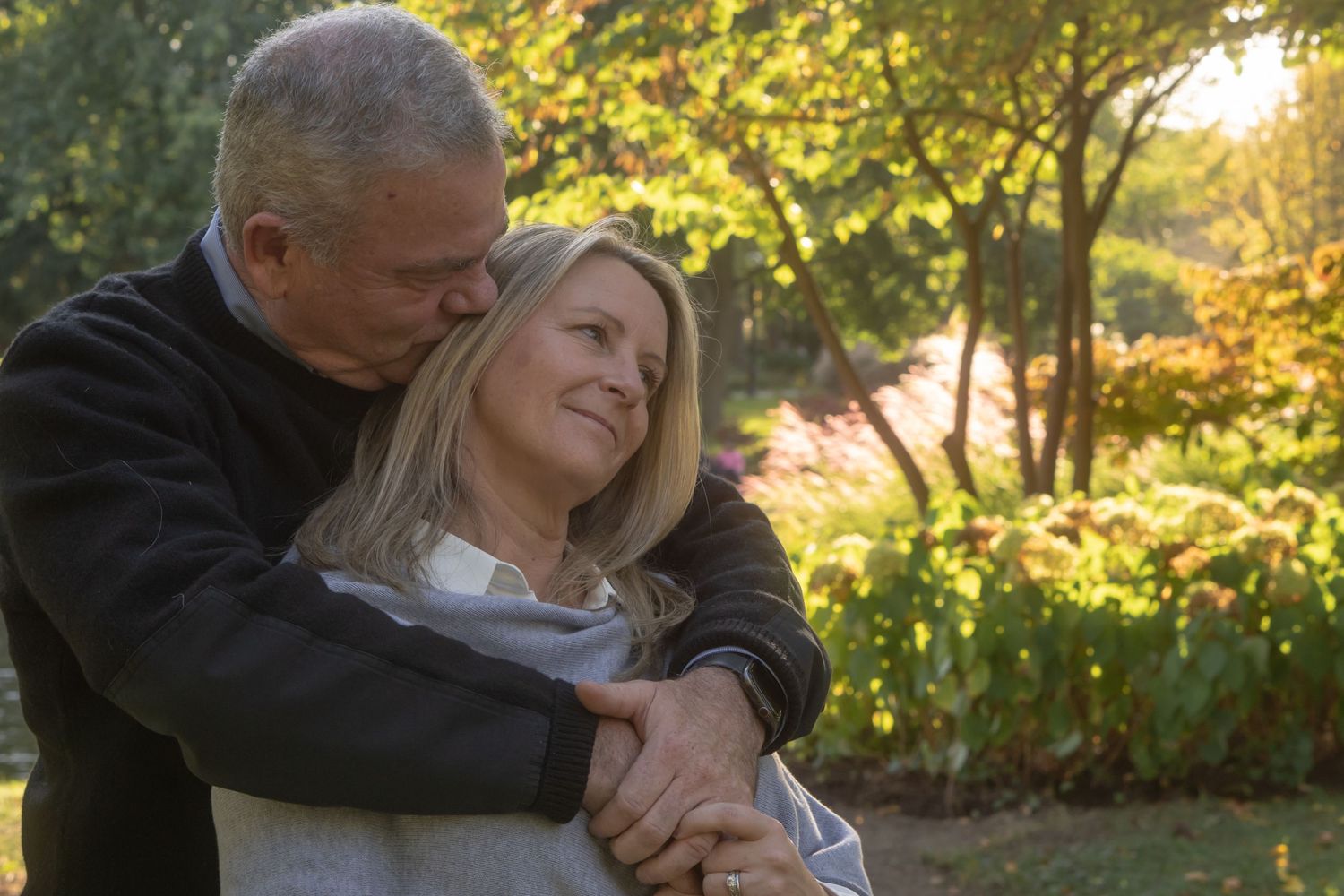 A couple embraces in a sunlit garden setting during a romantic outdoor photoshoot.