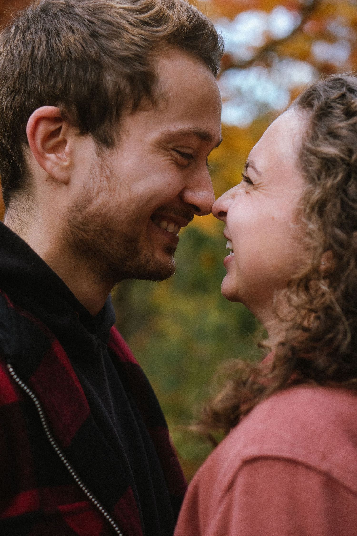 Couple sharing joyful laughter and intimate moment against autumn foliage.