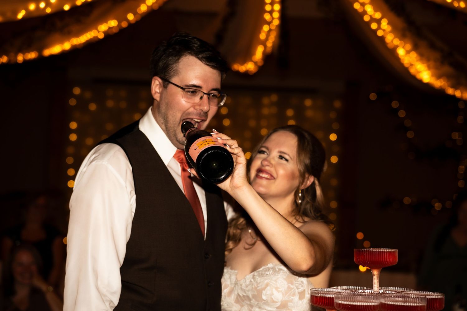 bride holds champagne bottle for the groom to drink