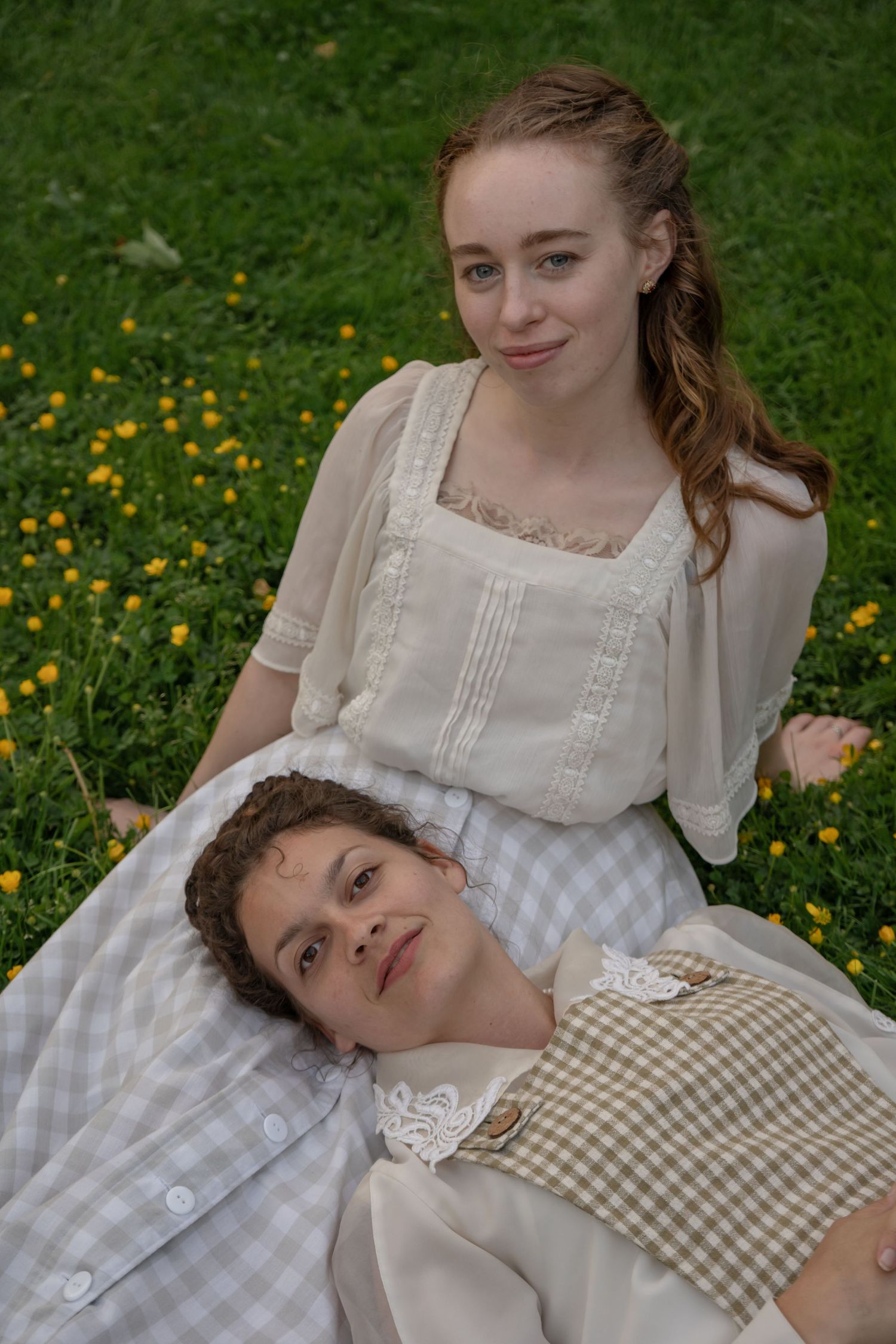 Romantic vintage-styled couple in period dress resting on checkered blanket among wildflowers.