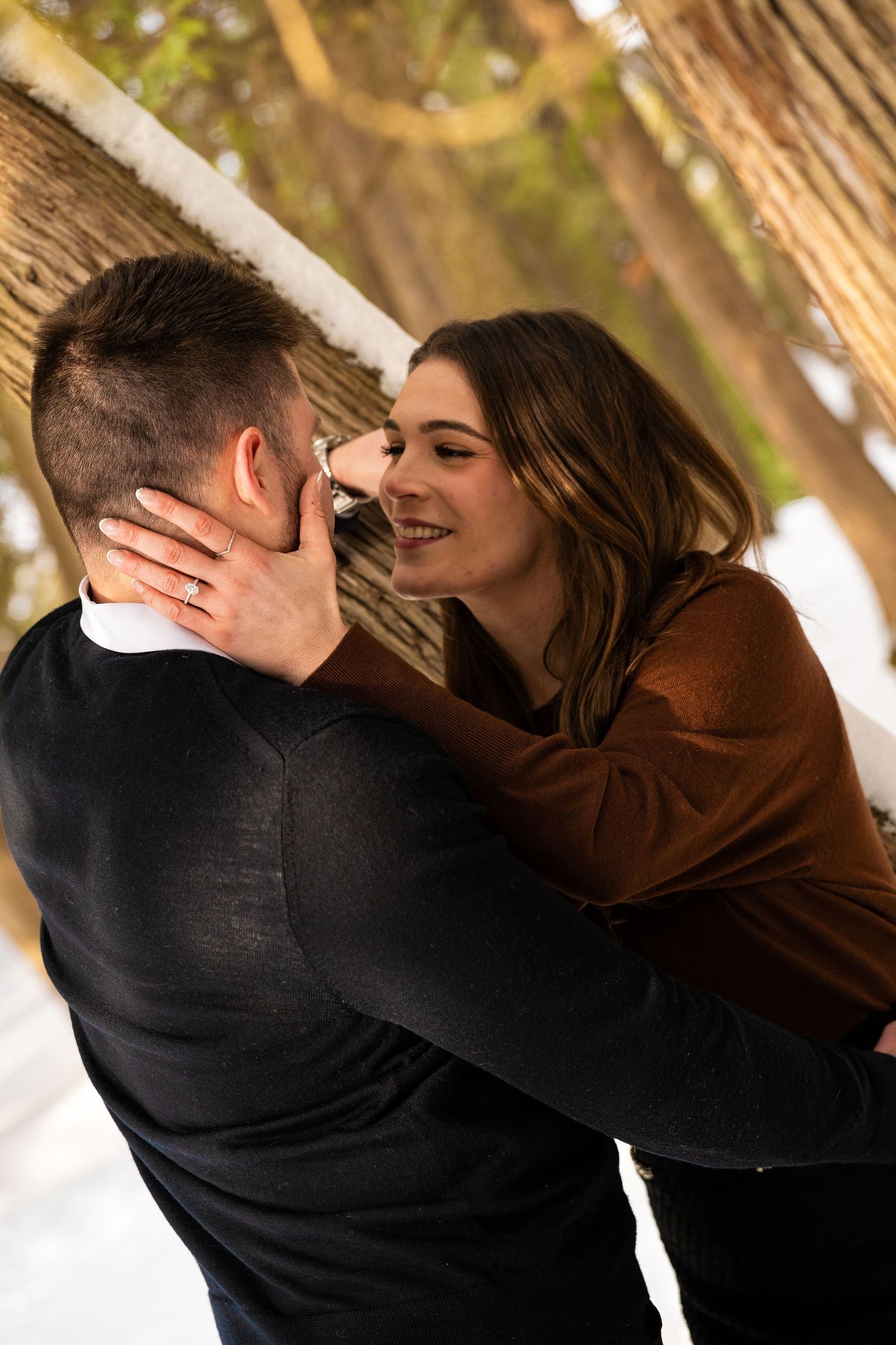 Man and women embrace while leaning against a tree.