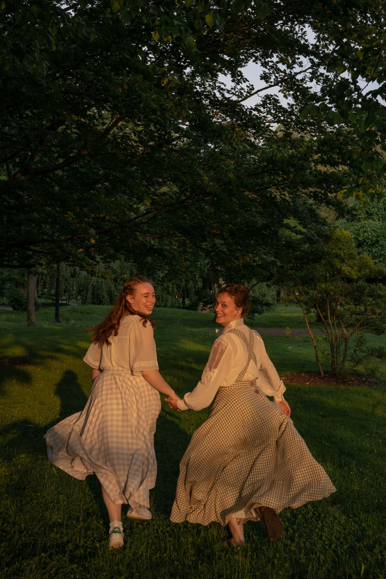 Two people in matching gingham dresses lay in green grass during golden hour.