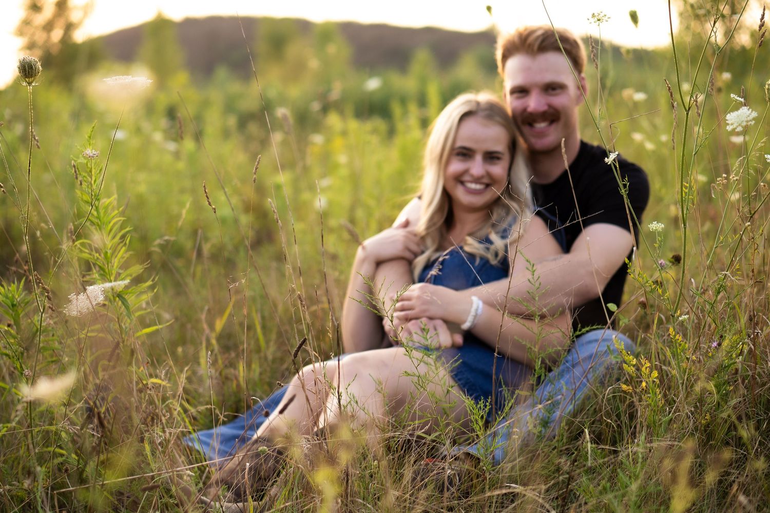 Couple sit together smiling at the camera in flower field