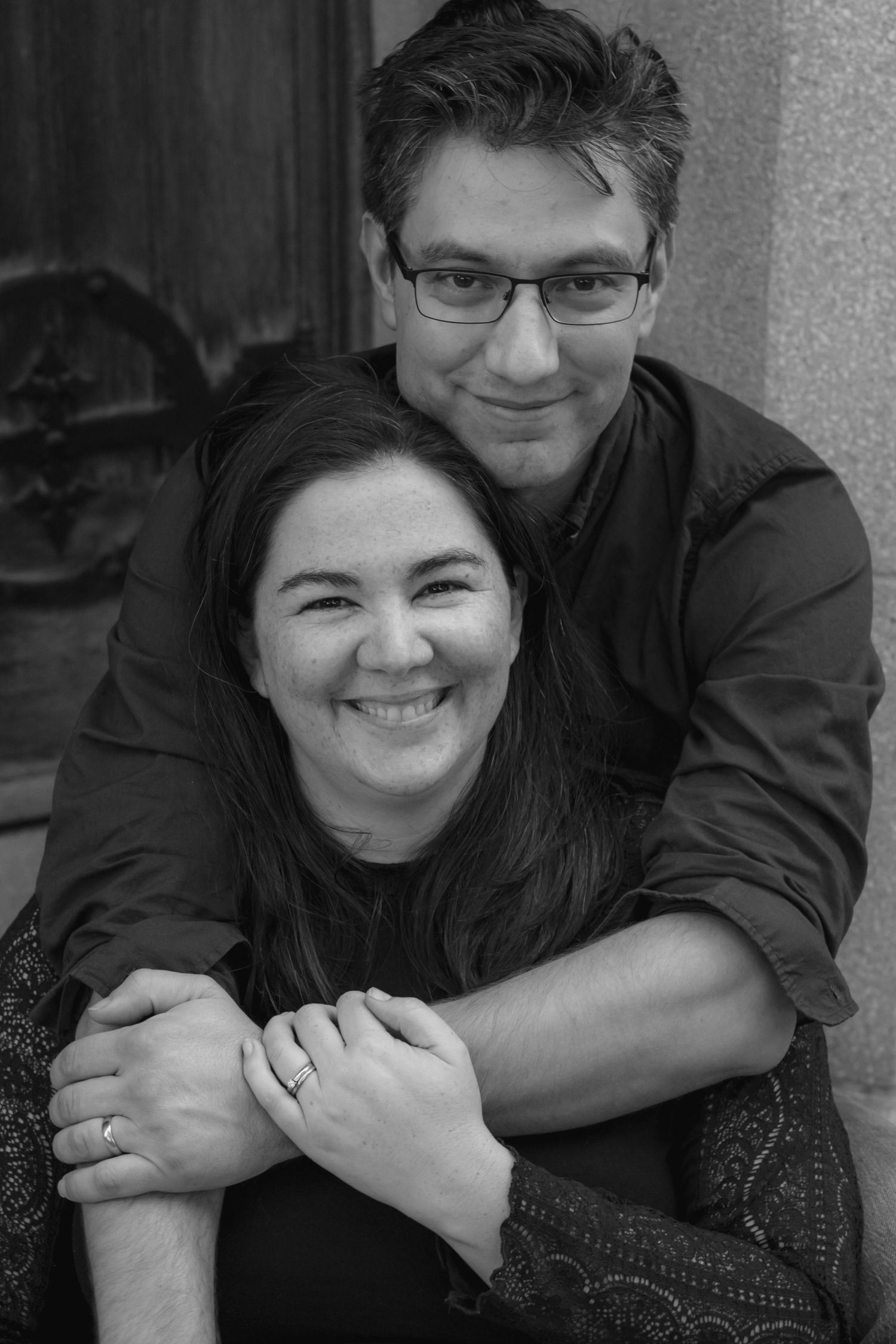 A black and white portrait of a happy couple embracing and smiling at the camera.