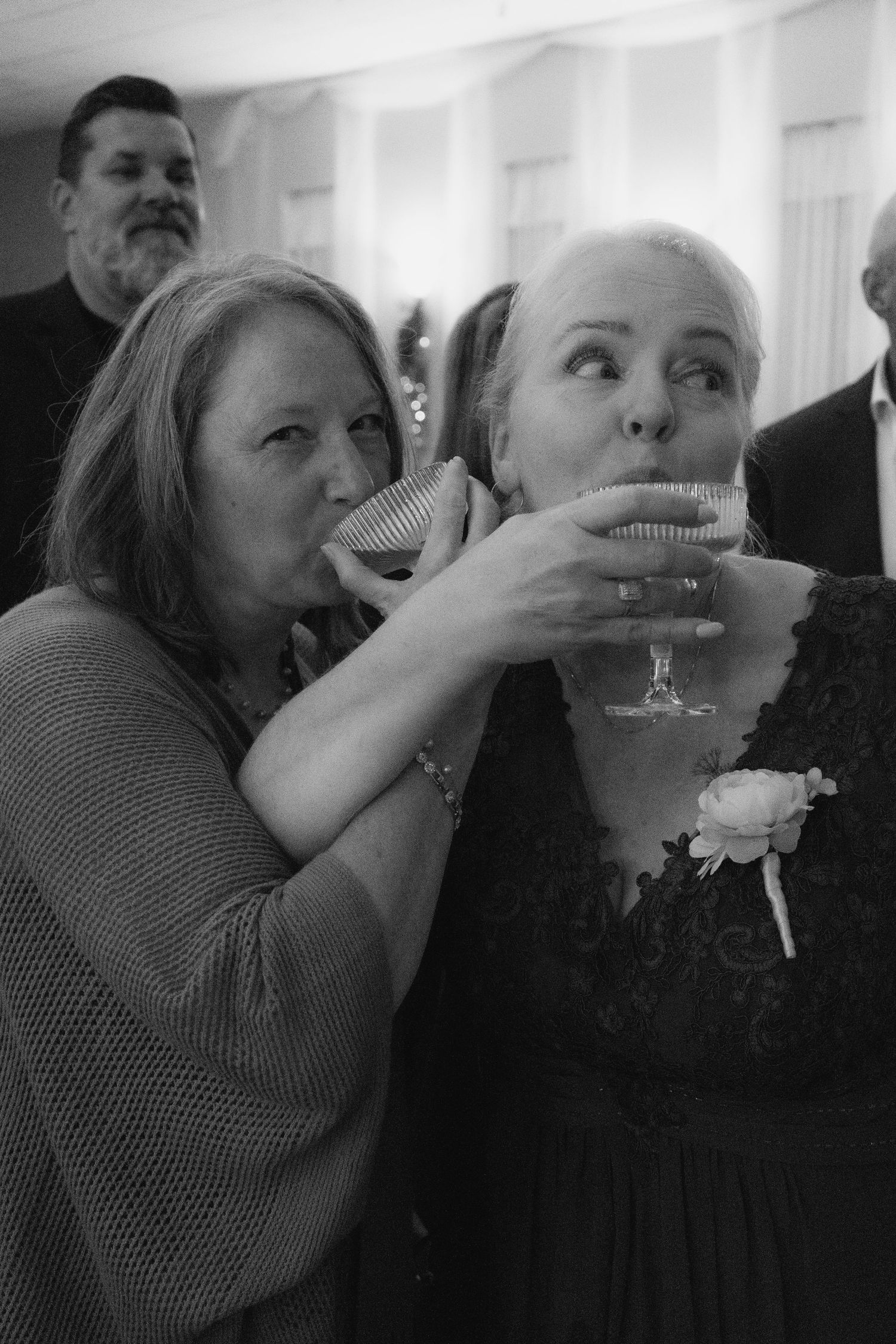 two women wrap arms around each other to drink