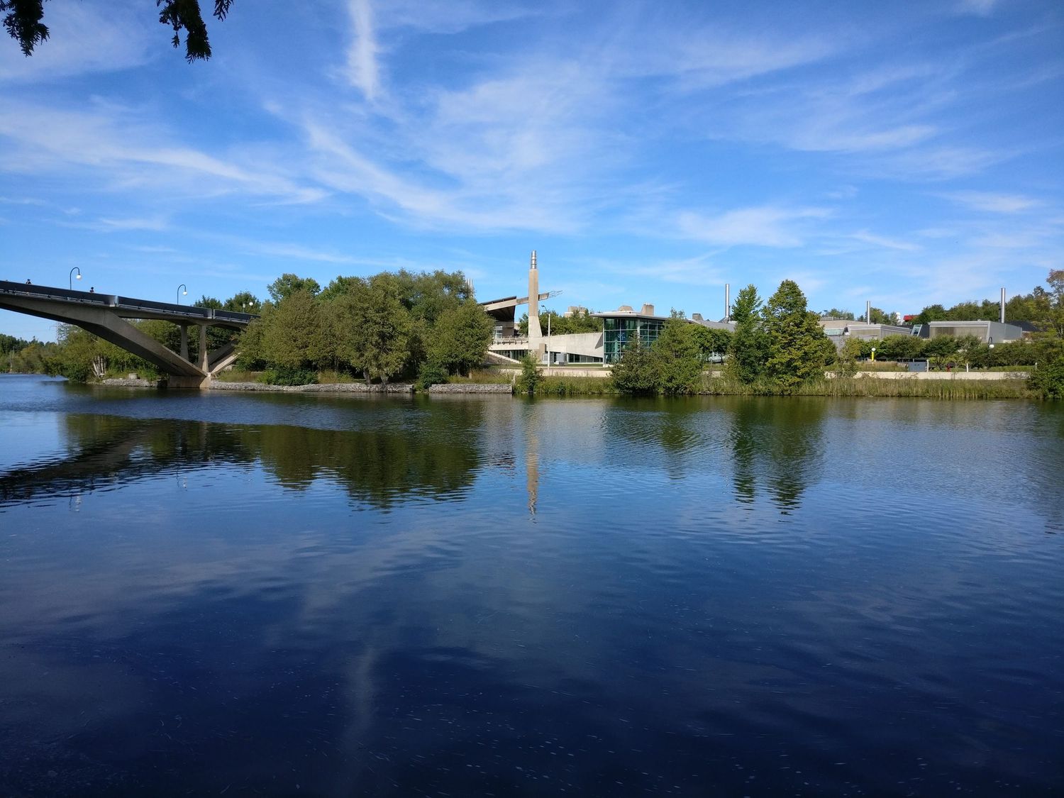 Panoramic view of a serene lake with blue skies and residential buildings along the shoreline.