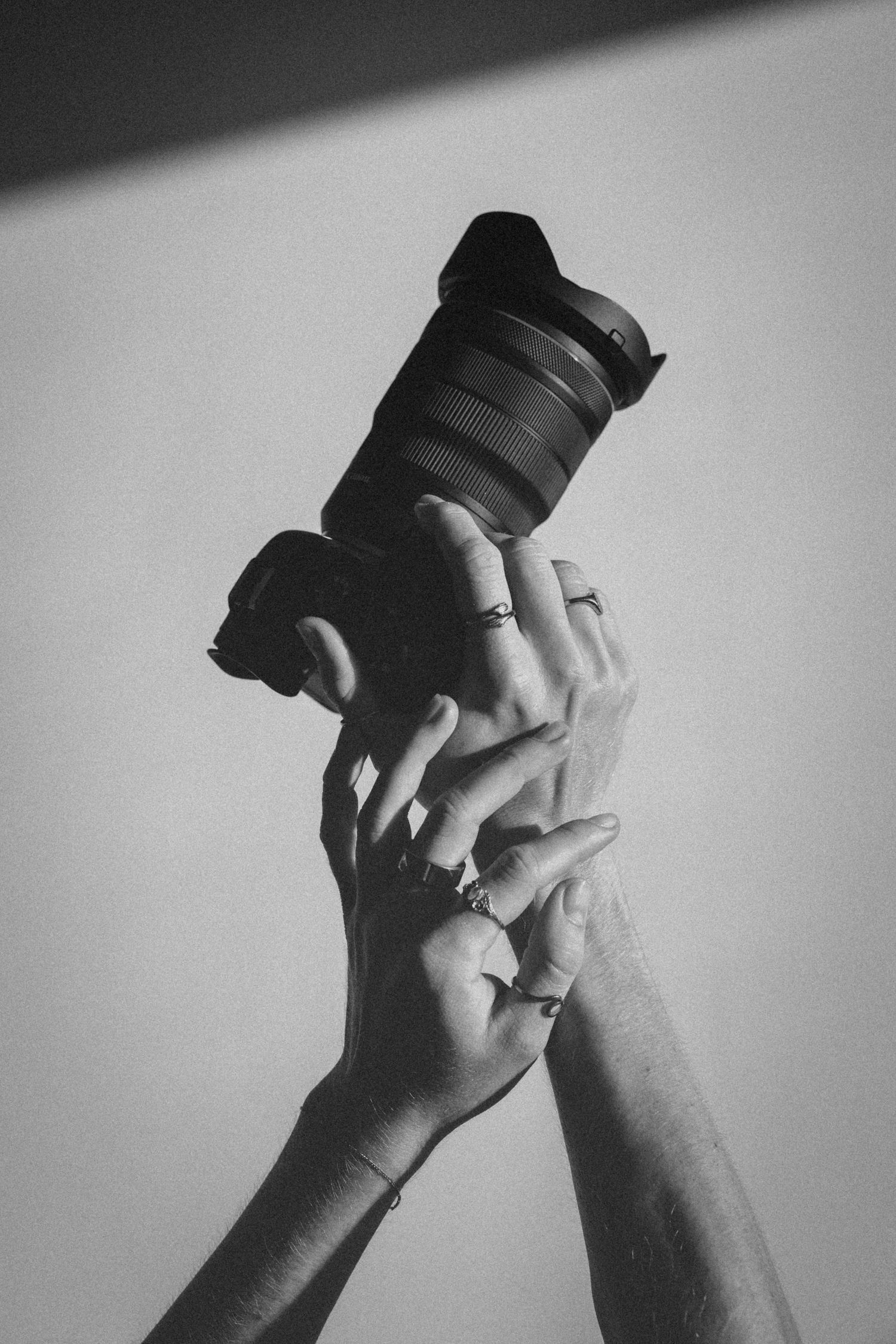 Black and white photo of two hands holding a DSLR camera with zoom lens against plain background.