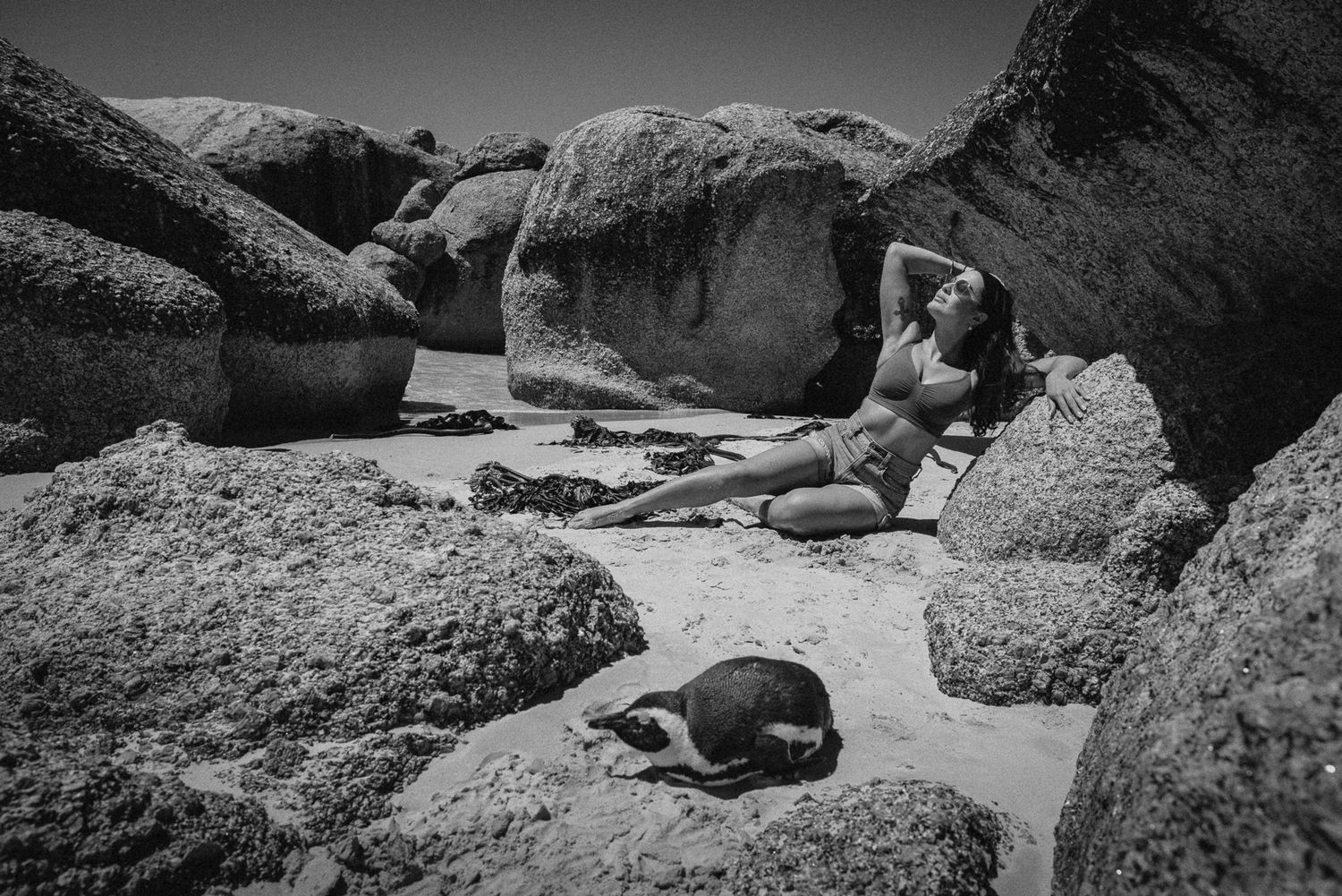 Black and white photo of woman in bikini resting on beach rocks.