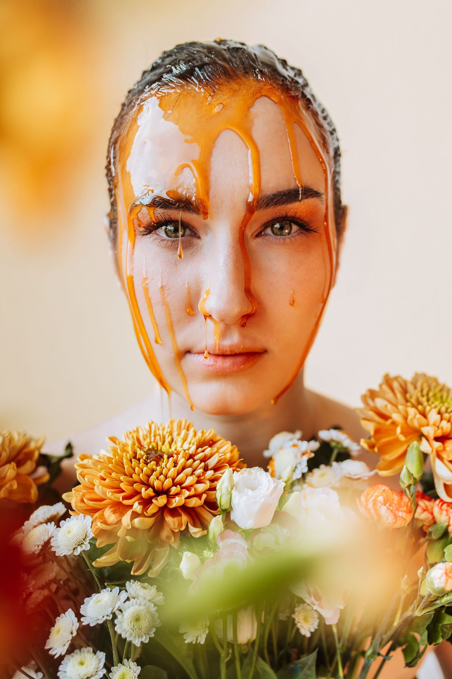 Young woman with honey dripping down her face holds a bouquet of orange and white chrysanthemums.