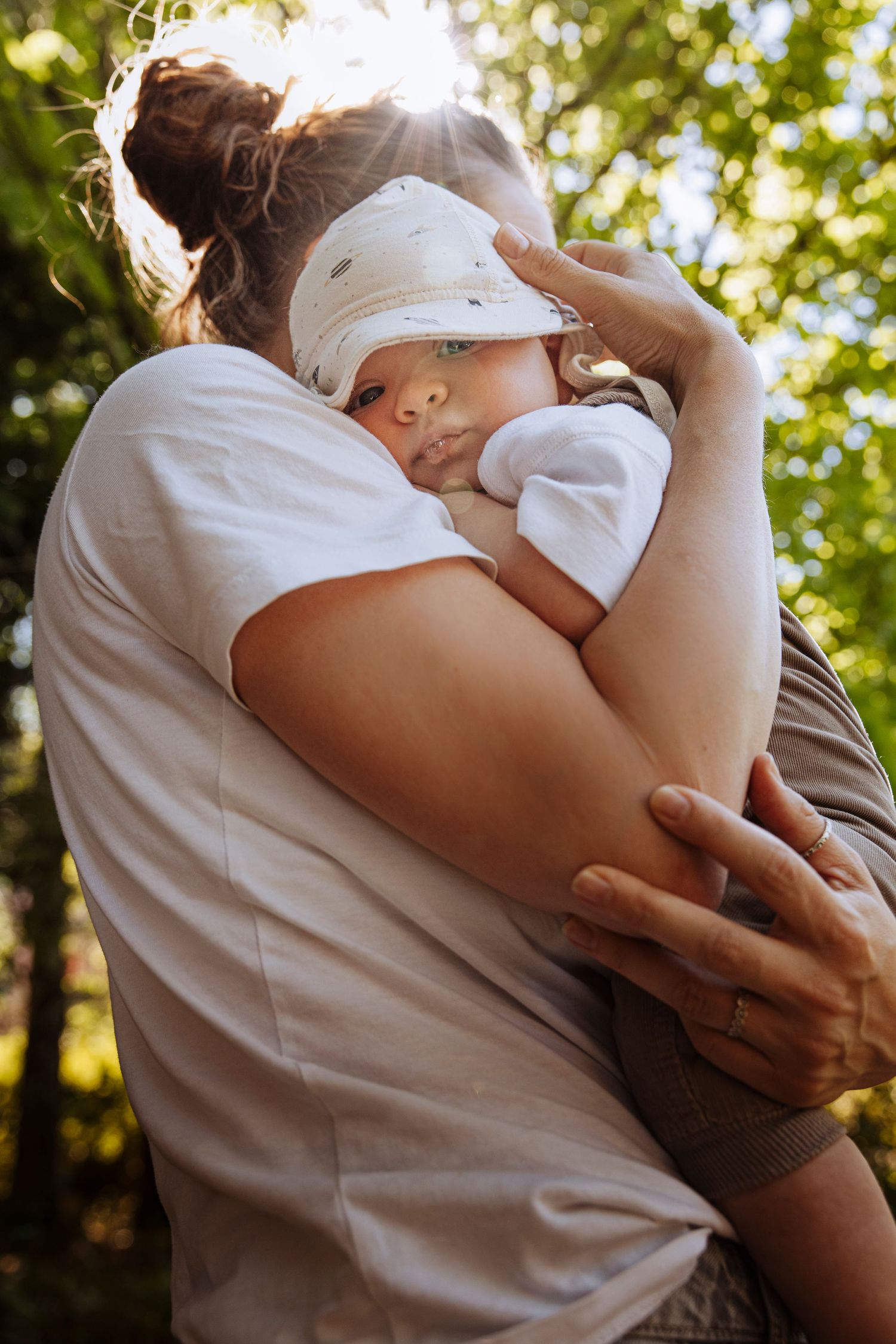 Mother tenderly holding her newborn baby against her shoulder in a sunlit green garden.