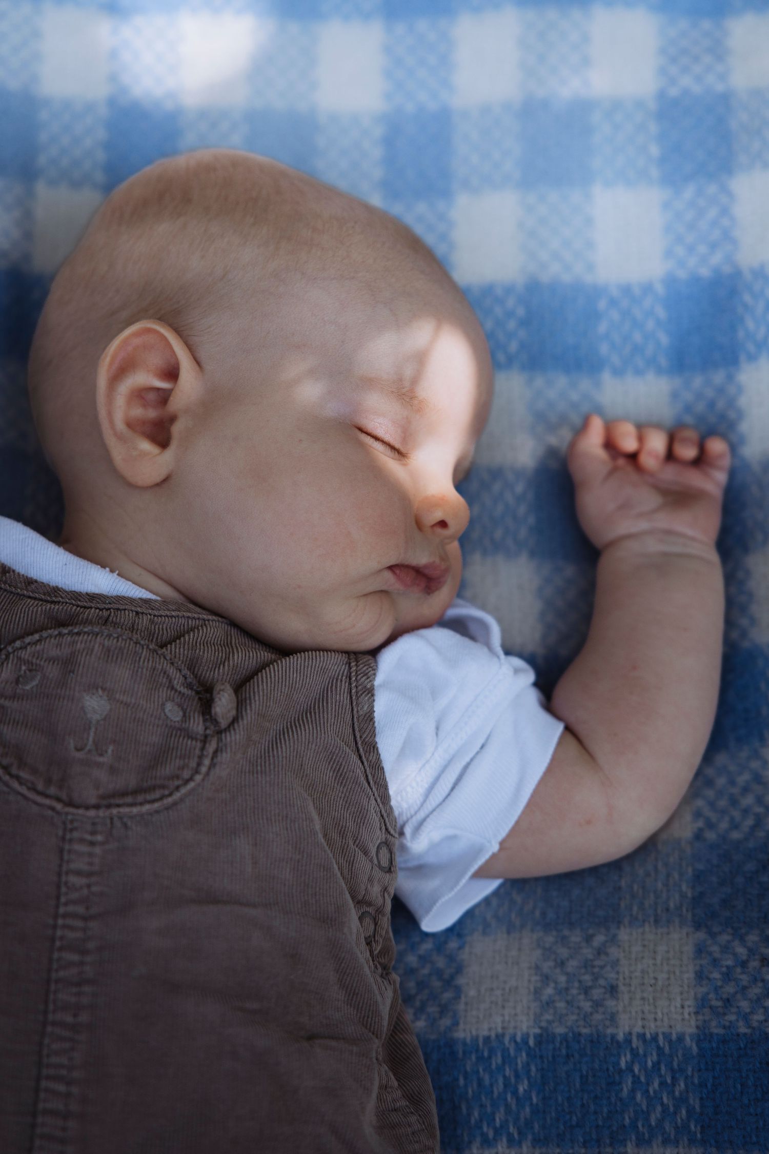 Peaceful newborn baby sleeping on a blue checkered blanket wearing a brown vest outfit.