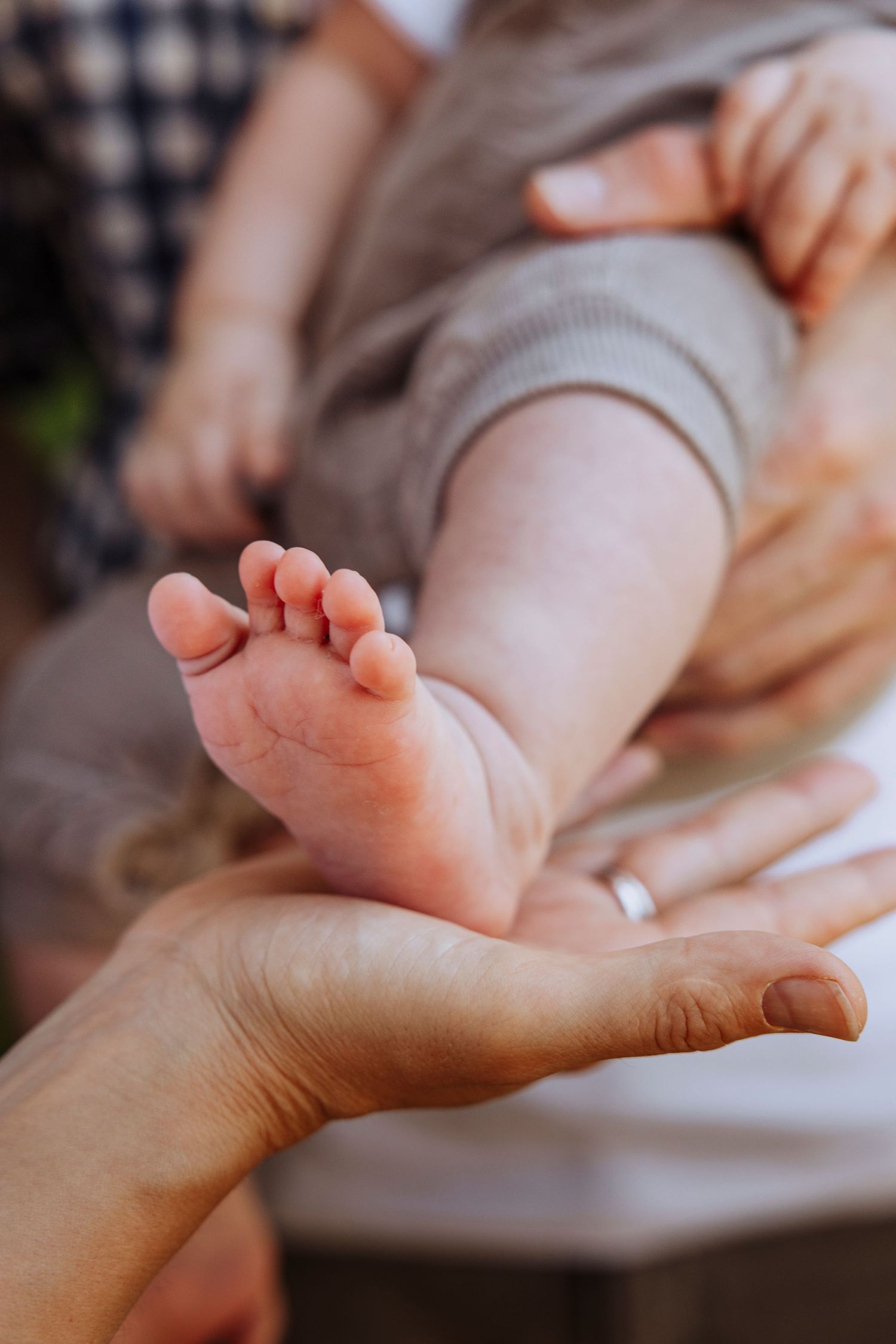 Close-up of a newborn baby's tiny feet resting gently in a parent's hand, with a wedding ring visible.