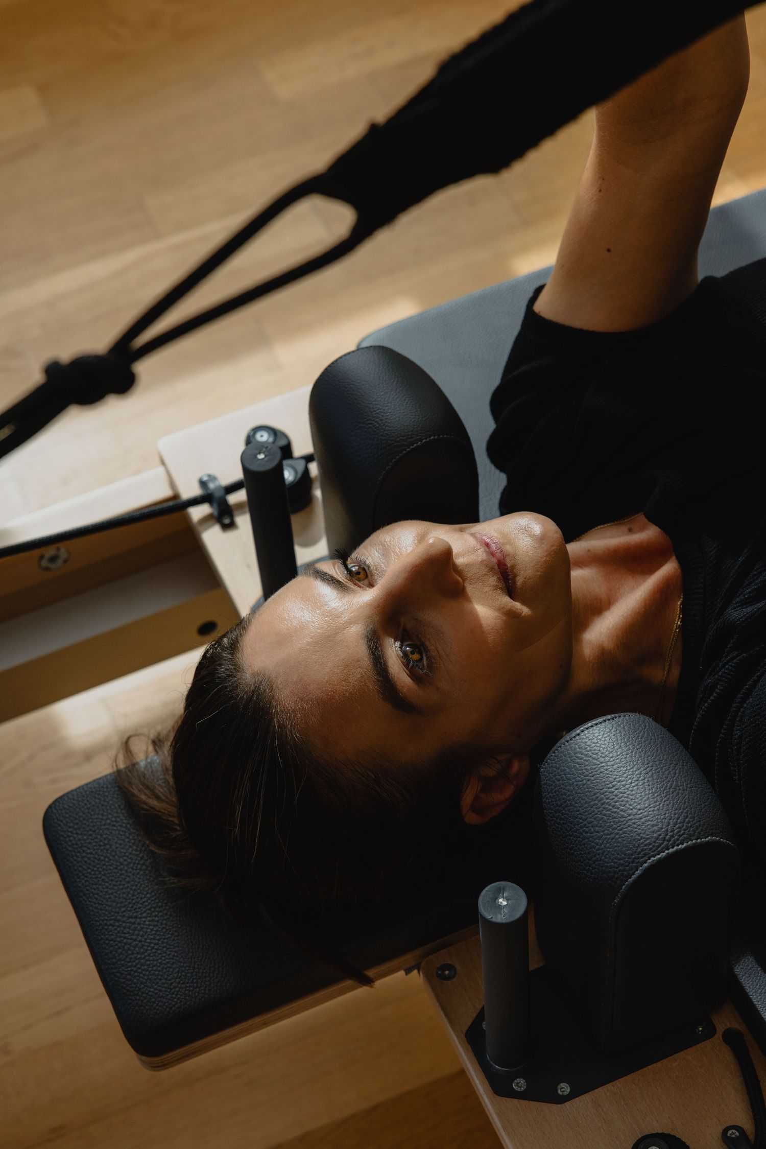 Woman lying on a Pilates reformer machine during a workout session in a modern fitness studio.