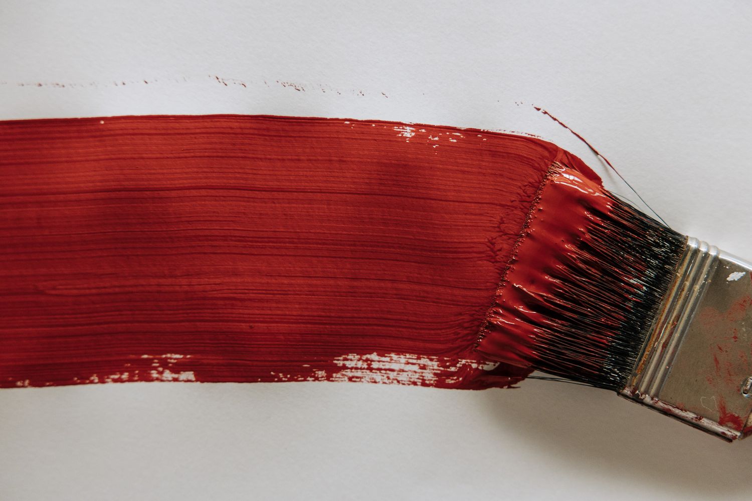A paintbrush applying a bold red paint stroke on a white surface, ideal for art and painting concepts.