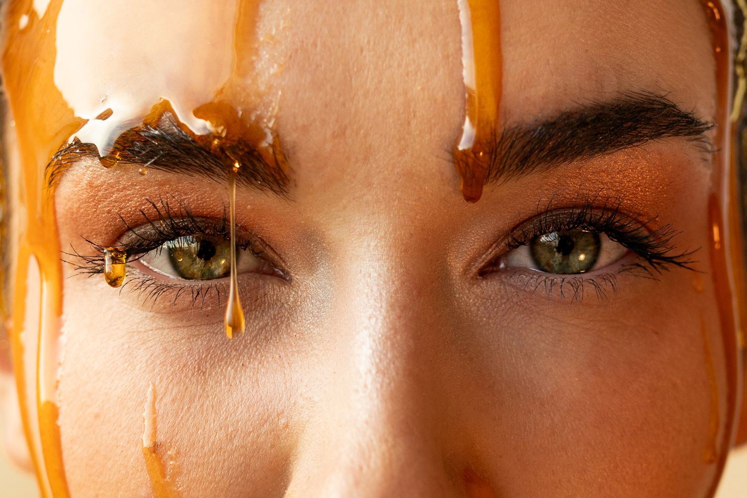 Close-up of woman's green eyes with golden honey dripping down her face in a beauty treatment concept.