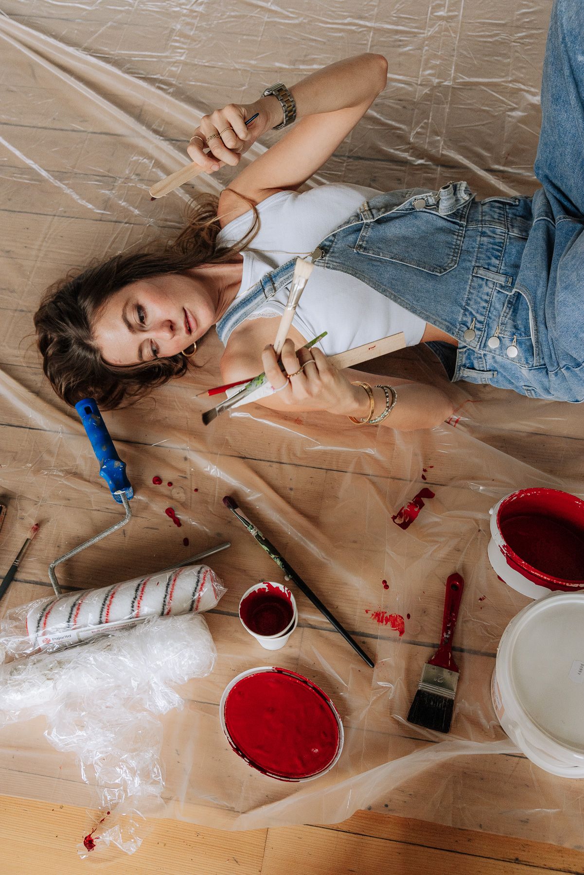 Young woman lying on drop cloth surrounded by red paint cans and brushes during a home renovation project.
