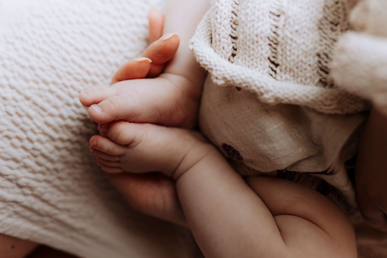 Close-up of tiny newborn baby feet resting on a soft knit blanket.