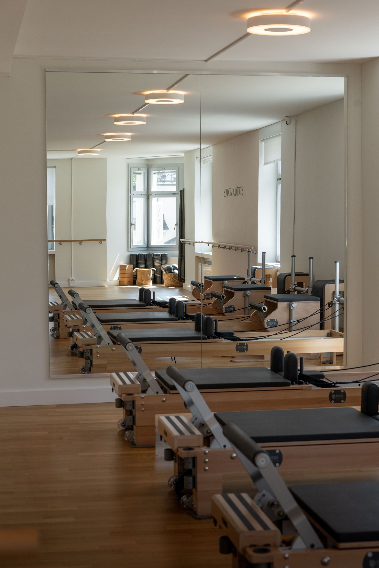 Modern Pilates studio with reformer machines lined up on hardwood floors, large mirrors, and elegant circular ceiling lights.