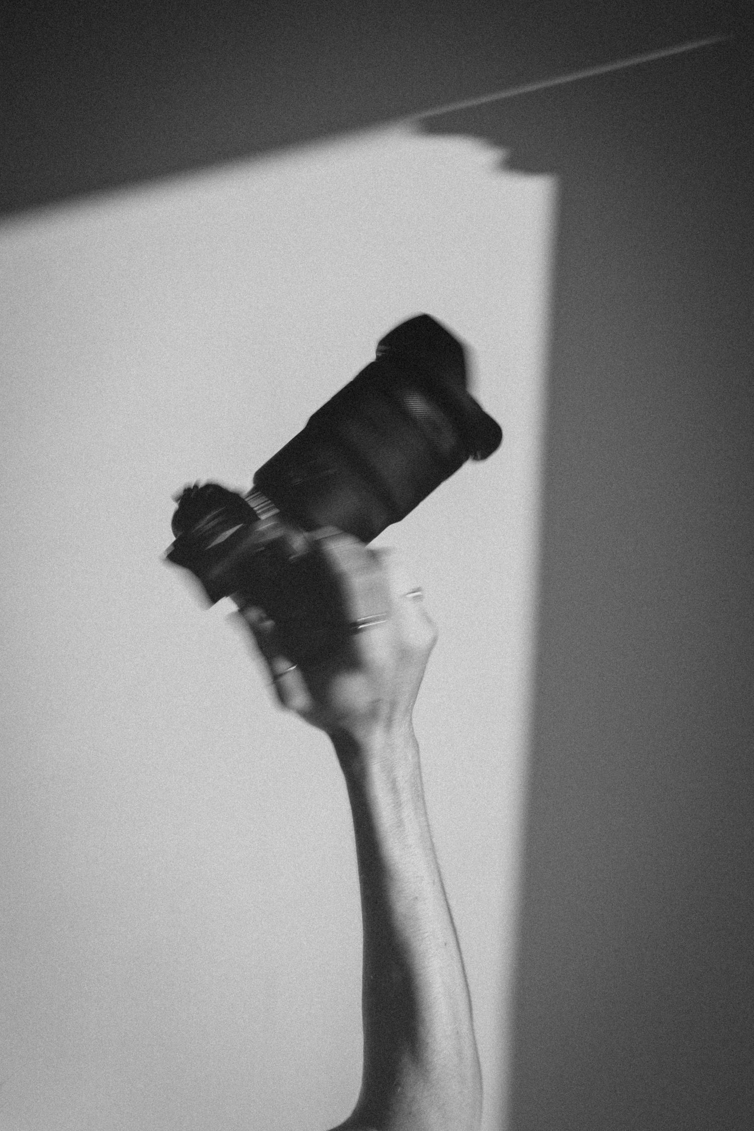 A hand raised holding a DSLR camera against a white wall with dramatic light and shadow in black and white.