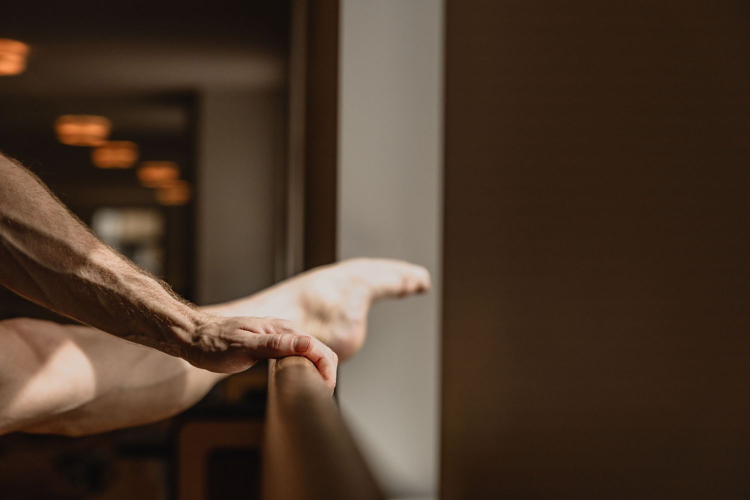 Close-up of a hand resting on a ledge in a softly lit hallway with warm glowing lights in the background.