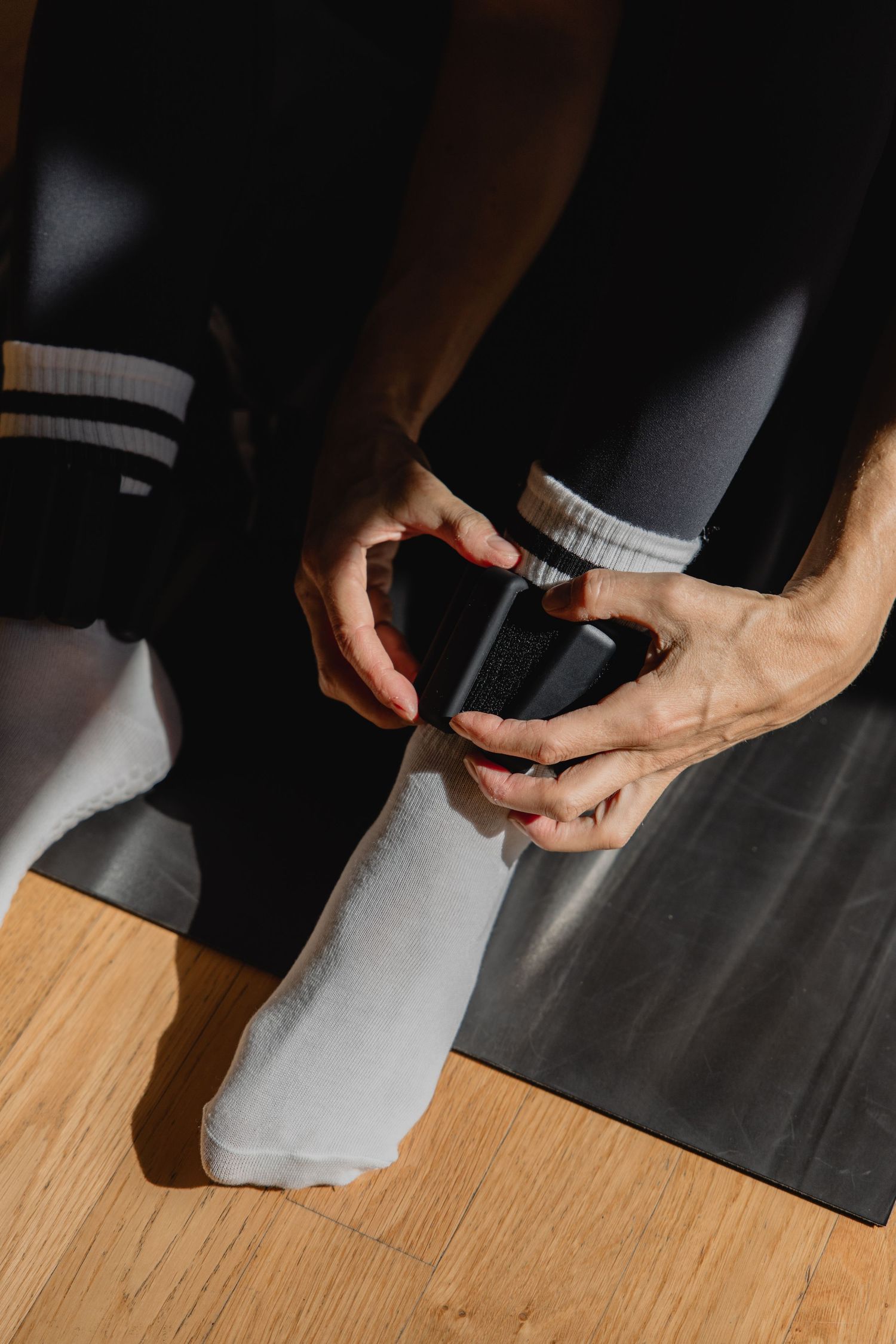 Person in athletic wear applying sports tape to ankle on yoga mat for injury support or prevention.