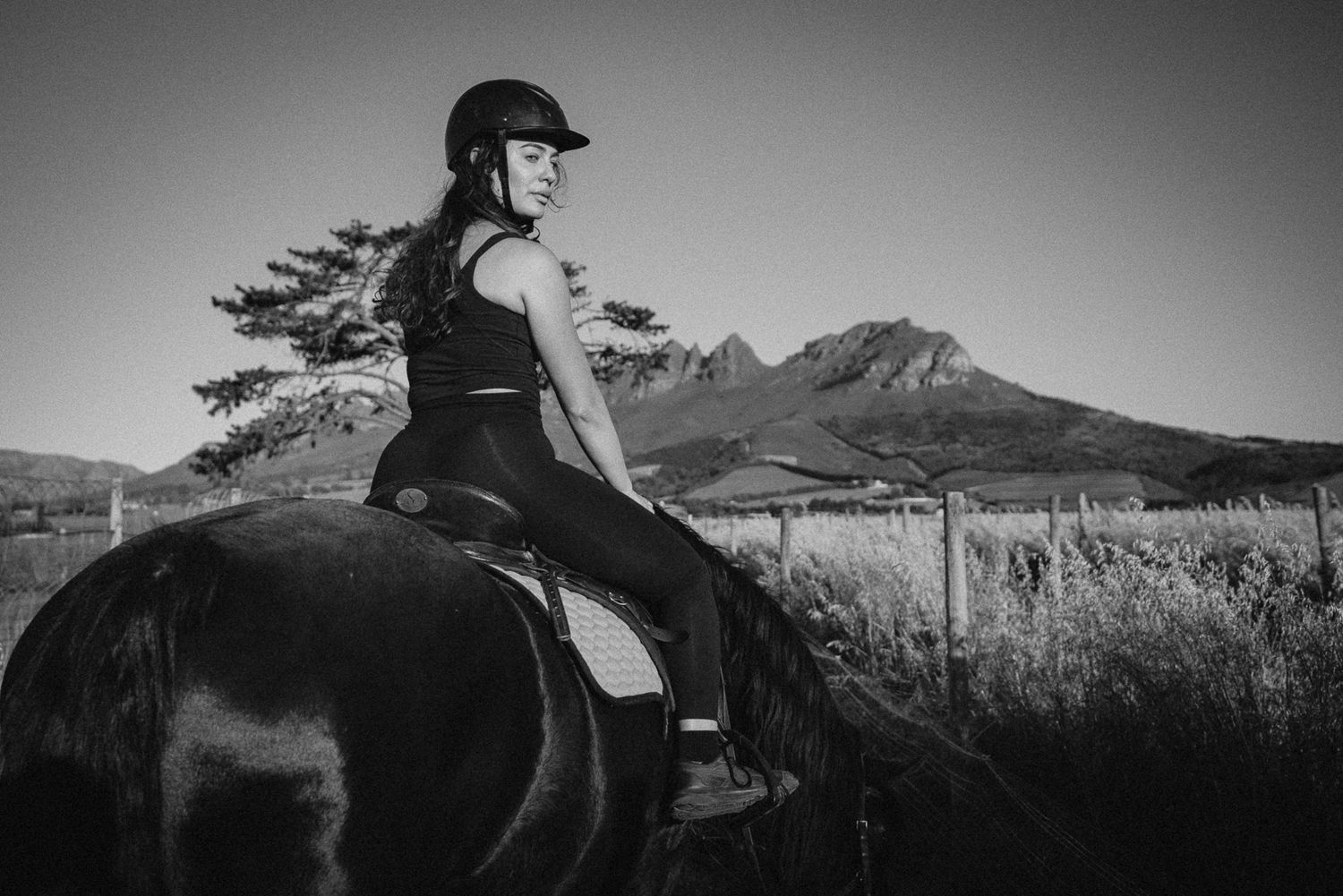 Black and white photo of woman riding horse with mountain view.