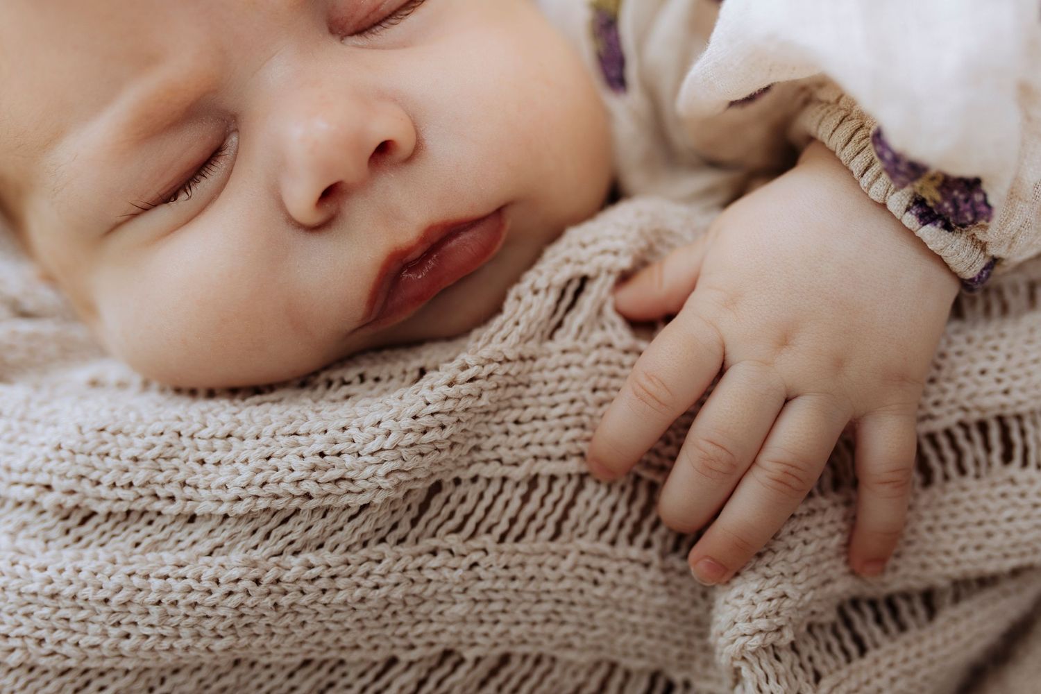 Close-up of a peacefully sleeping newborn baby wrapped in a soft beige knit blanket.