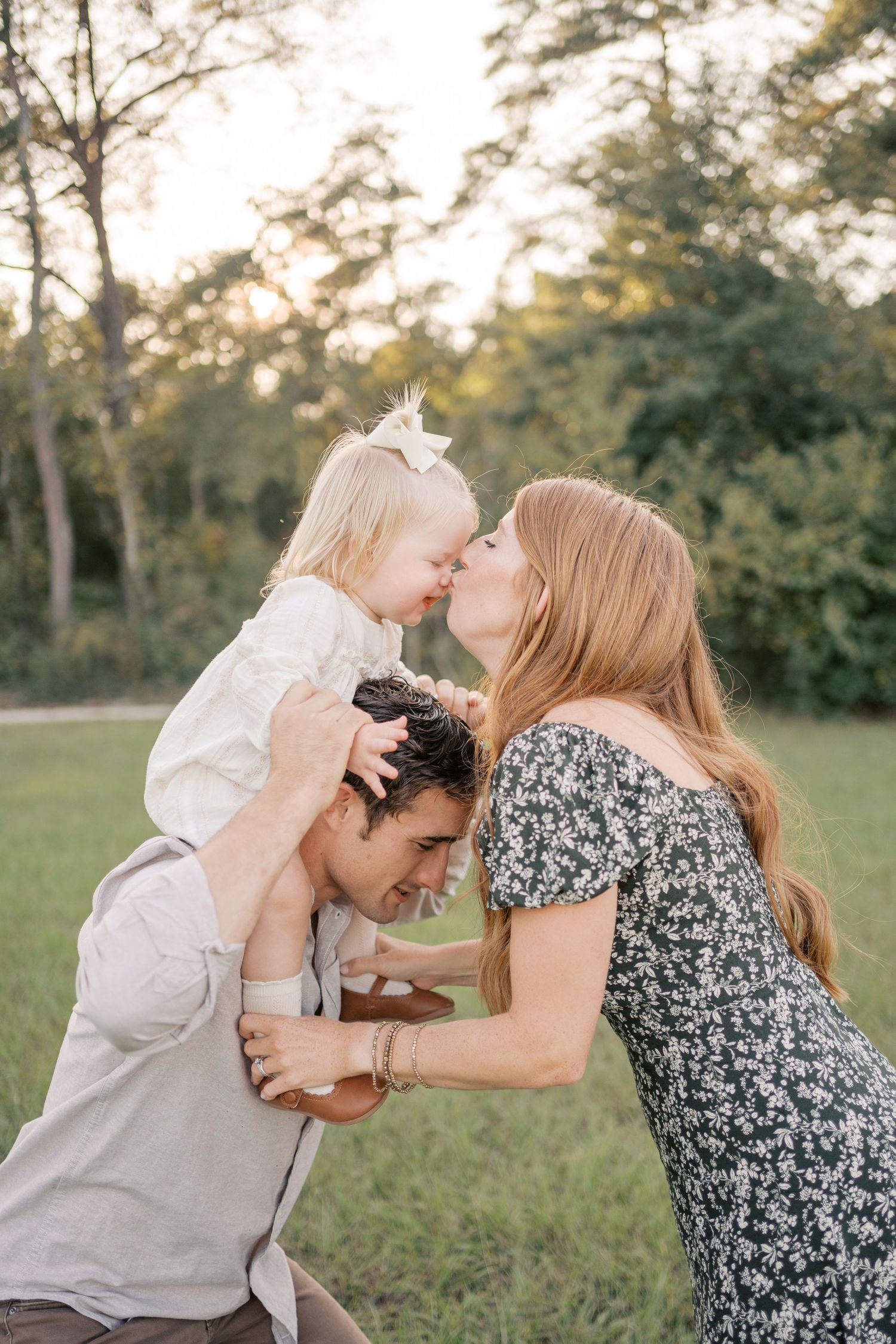 A loving family shares playful kisses and embraces while sitting together in a grassy field at sunset.