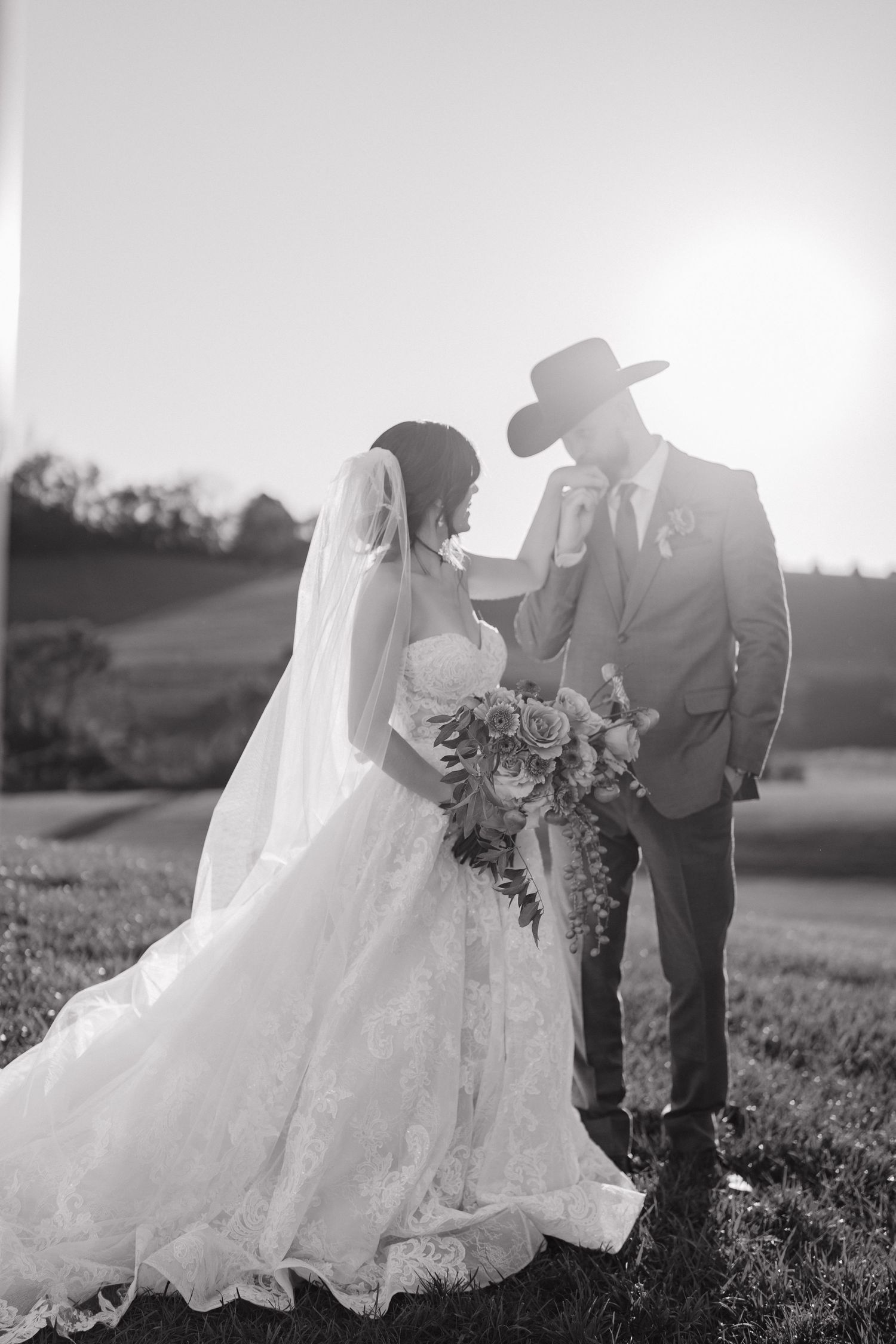 A romantic black and white wedding photo series showing a couple in a field at sunset with flowing white dress and veil.