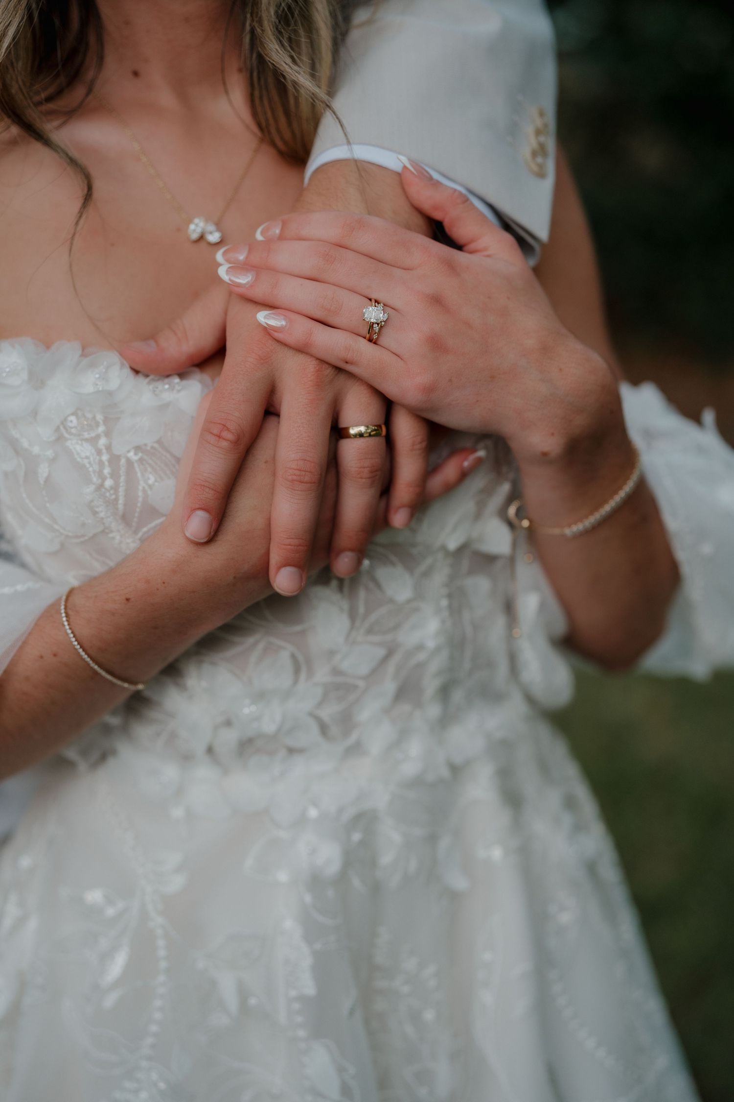 Close-up of newlyweds' hands showing wedding rings against white lace dress.