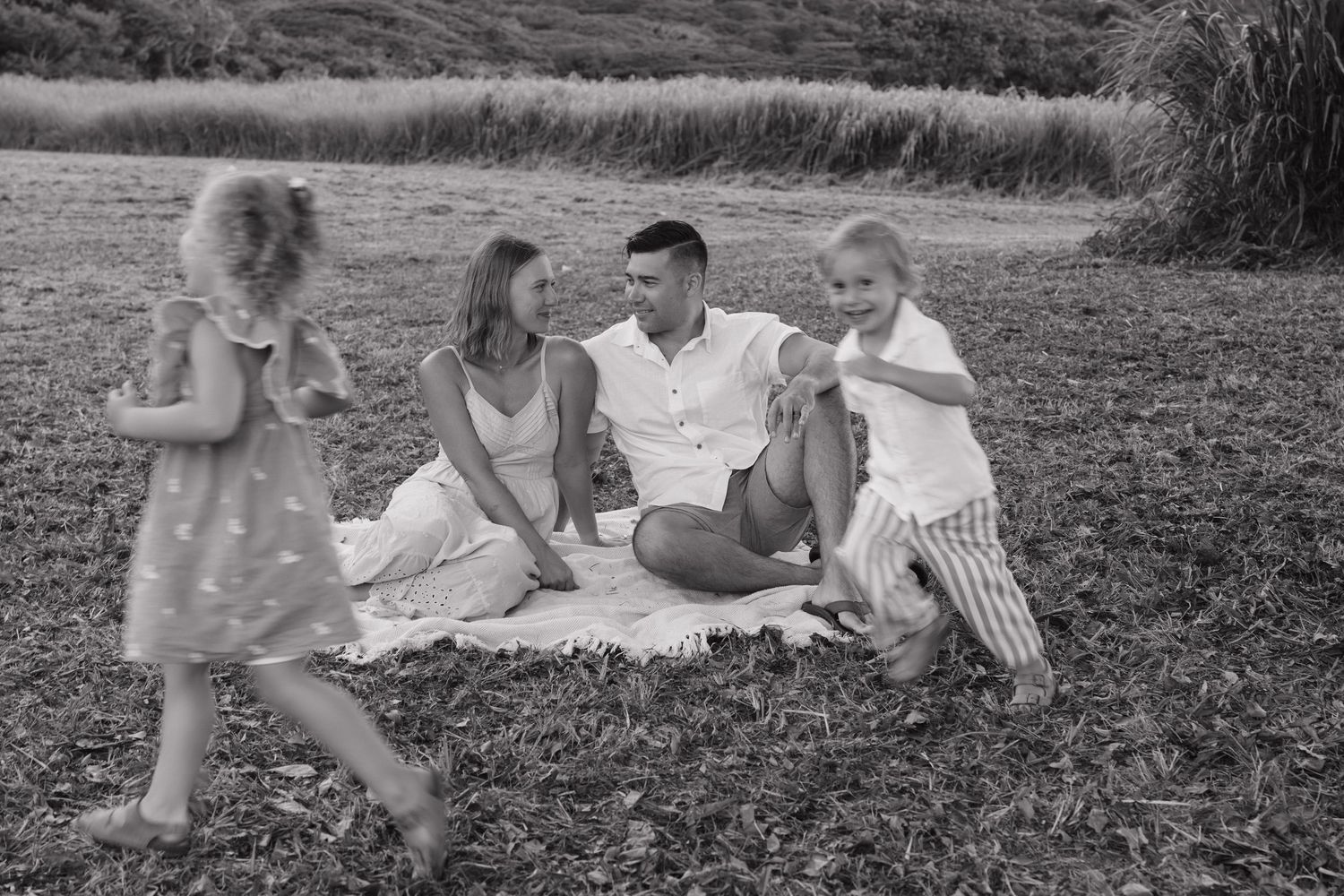 Black and white family photo of parents and two young children enjoying a picnic on grass in a park.