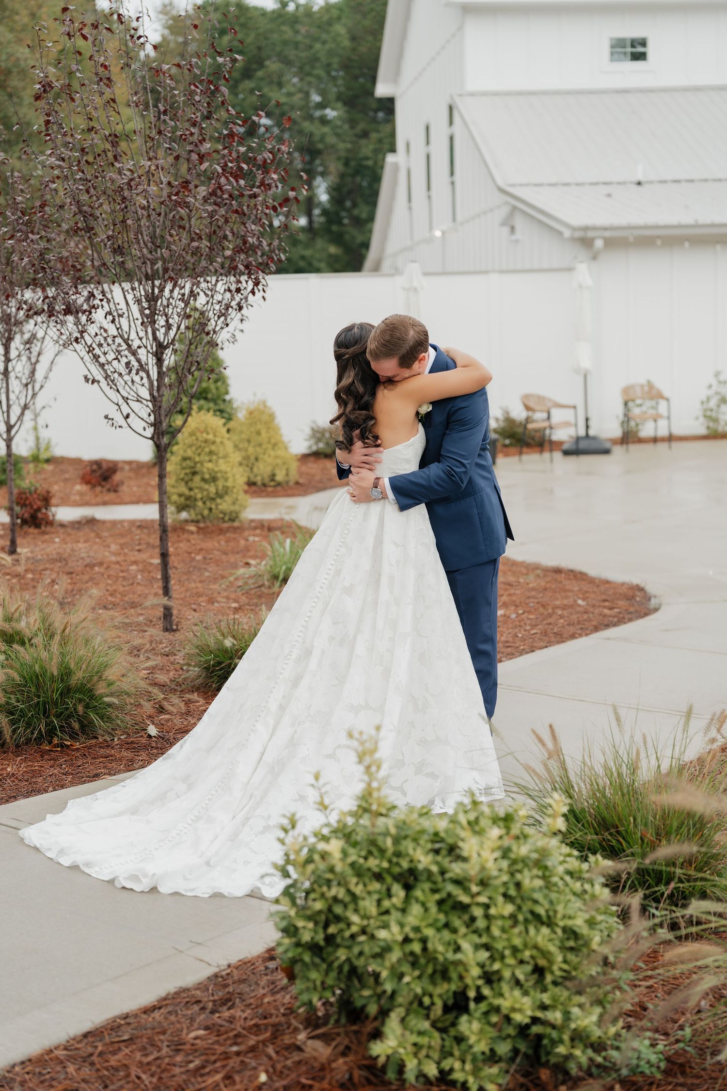 A bride and groom share intimate dance poses in front of a white chapel surrounded by landscaping.