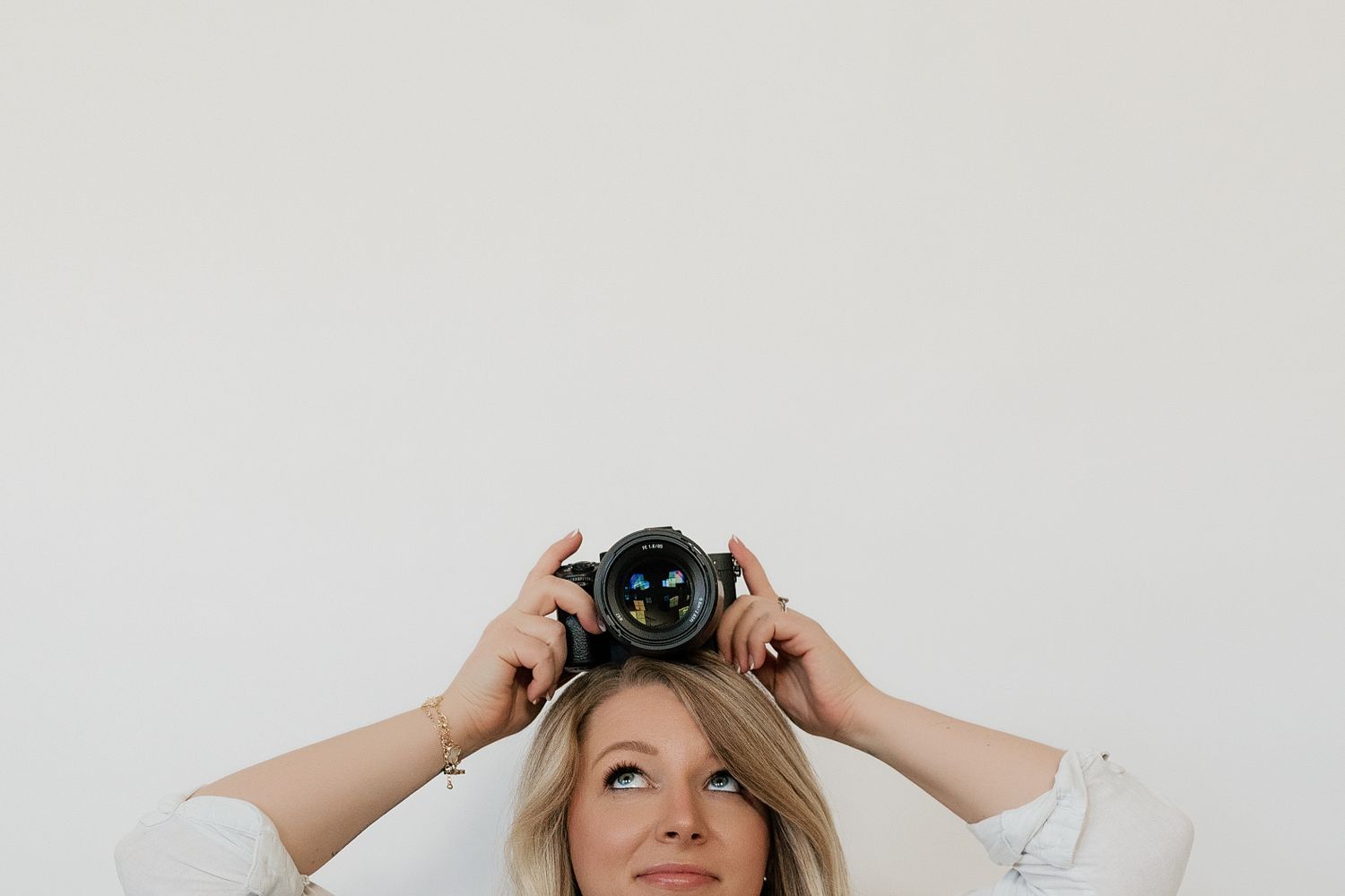 A person holds a vintage camera up to their face while looking upward in a light-filled setting.