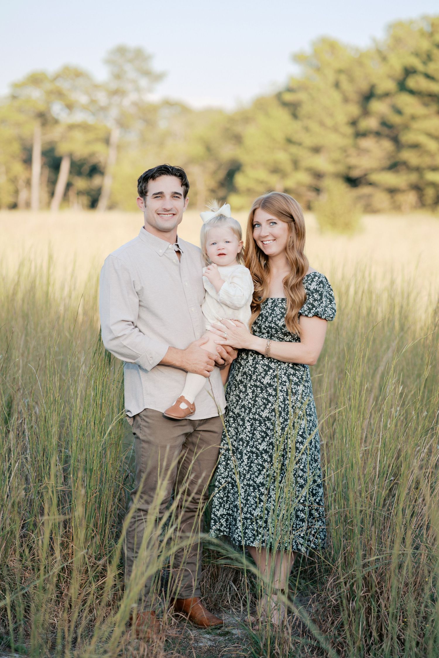 A family portrait in tall grass with sunset lighting and pine trees in the background.