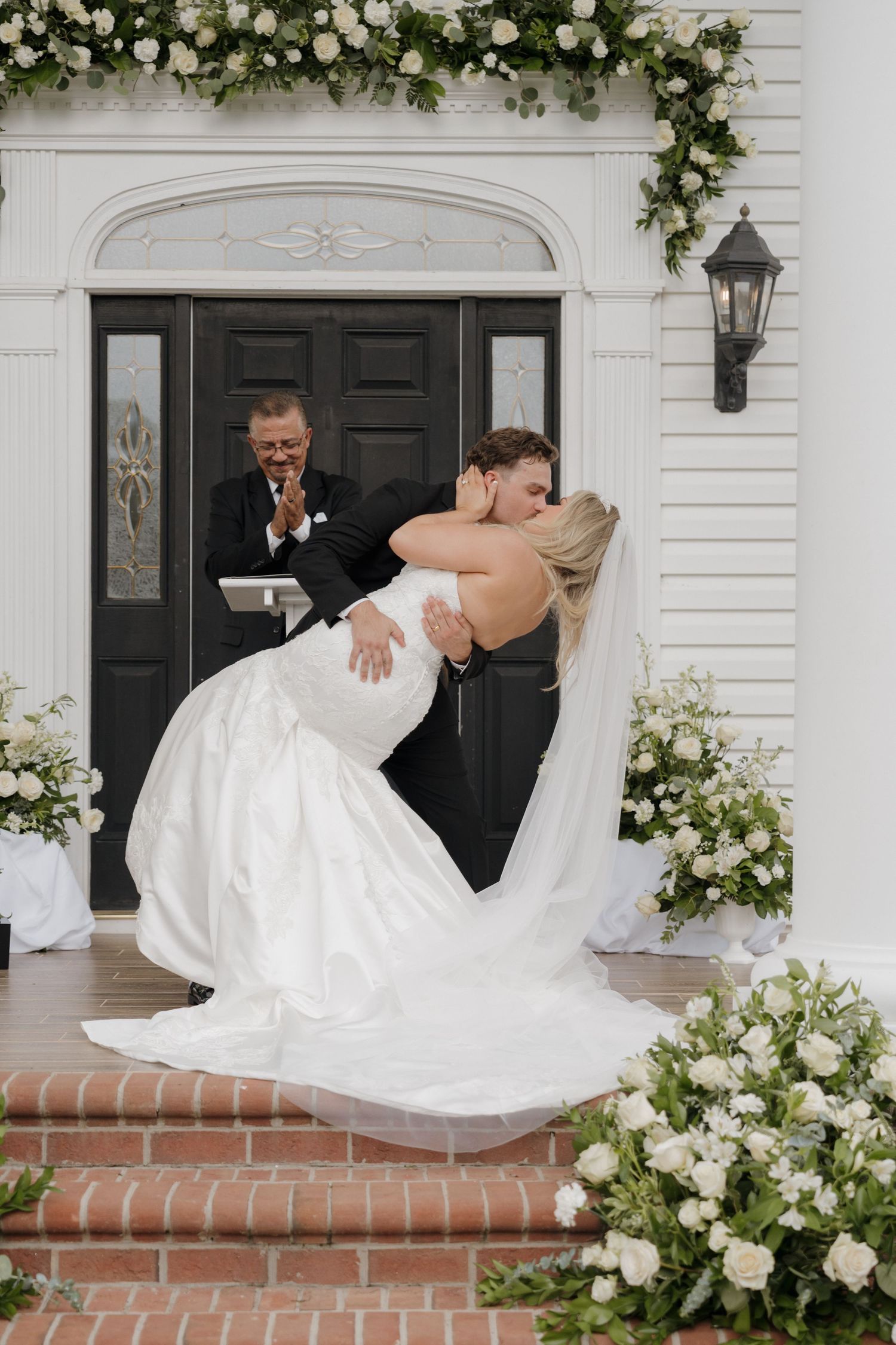 A romantic wedding moment with white floral decor and classic black door at a traditional church entrance.
