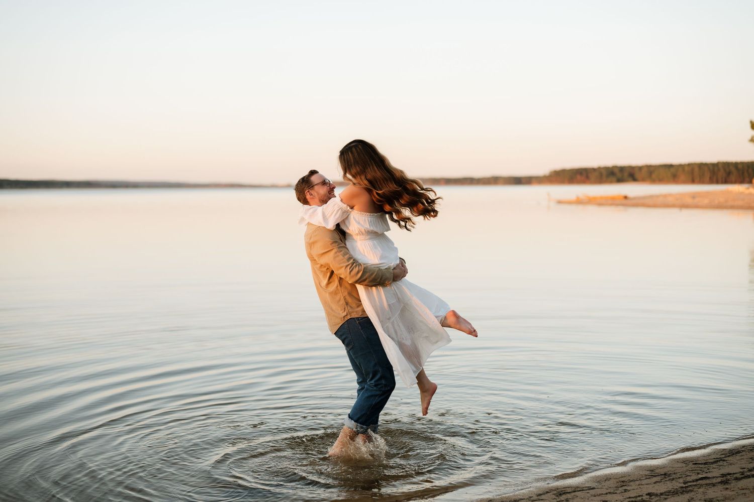 Two people playfully splash in calm lake waters at sunset creating ripples across the golden-lit surface.