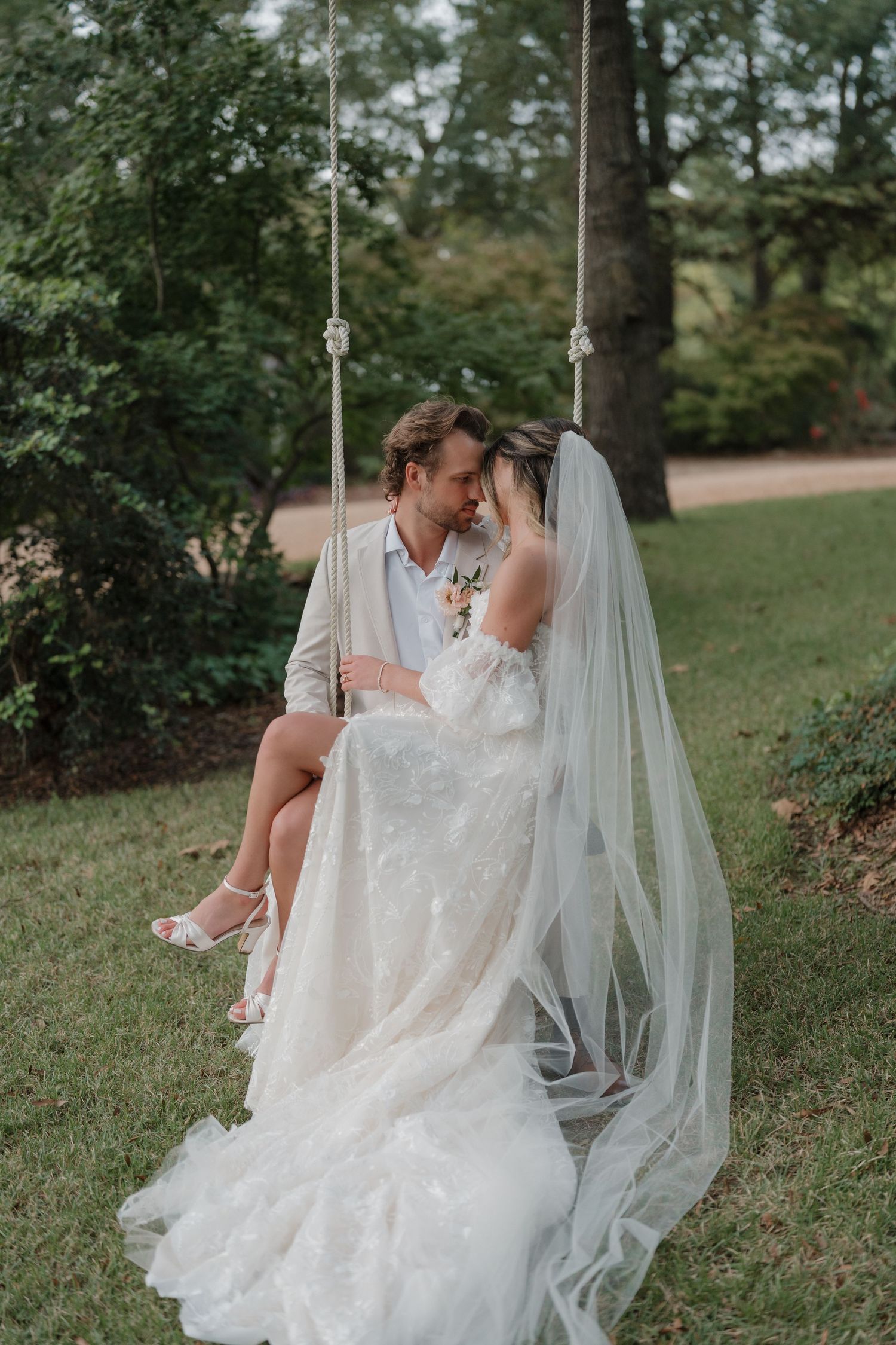 A romantic outdoor wedding scene with a flowing white bridal gown and veil against a lush green garden backdrop.