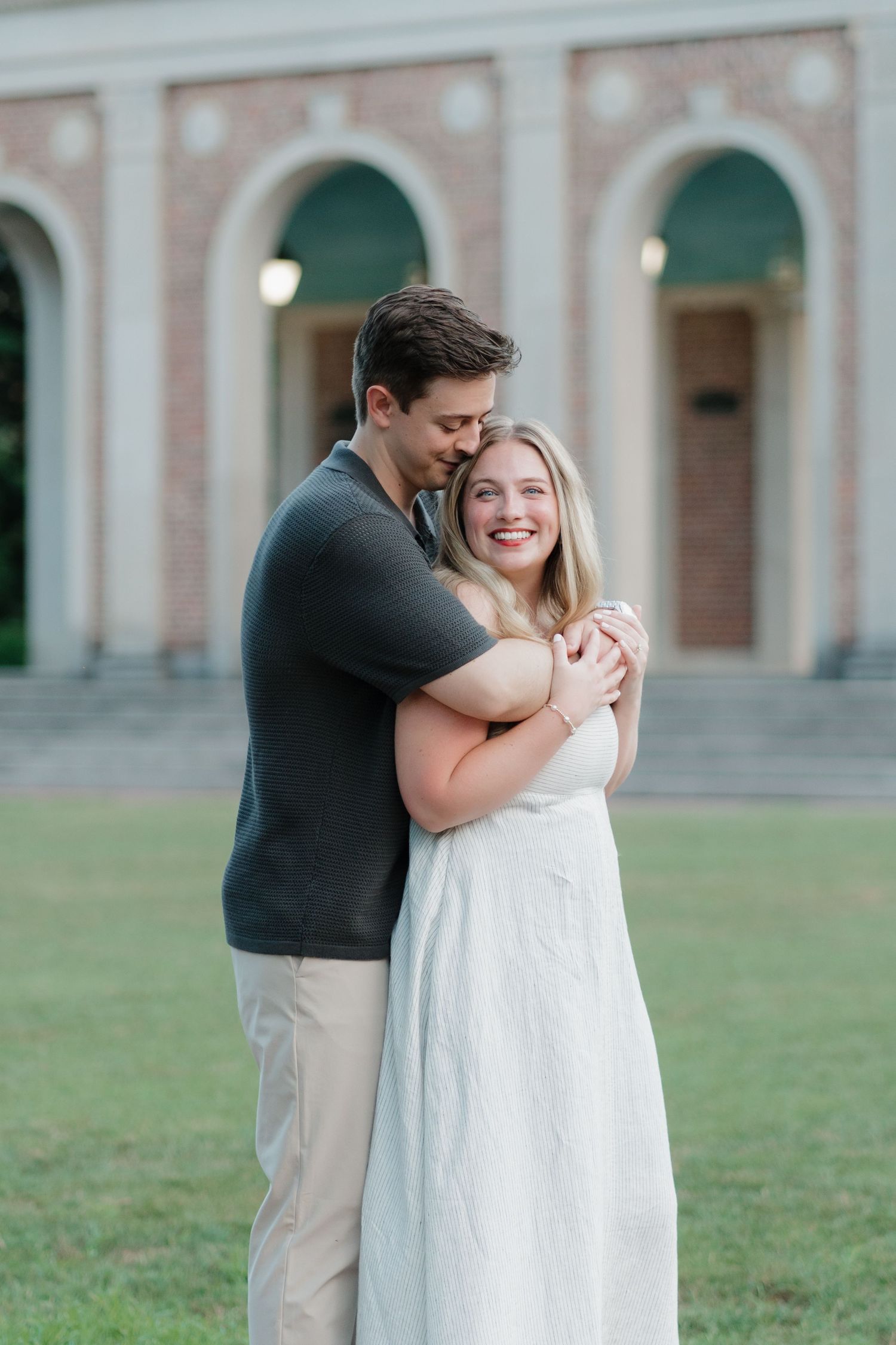 A couple shares a romantic moment in front of a stately brick building during an engagement photo session.
