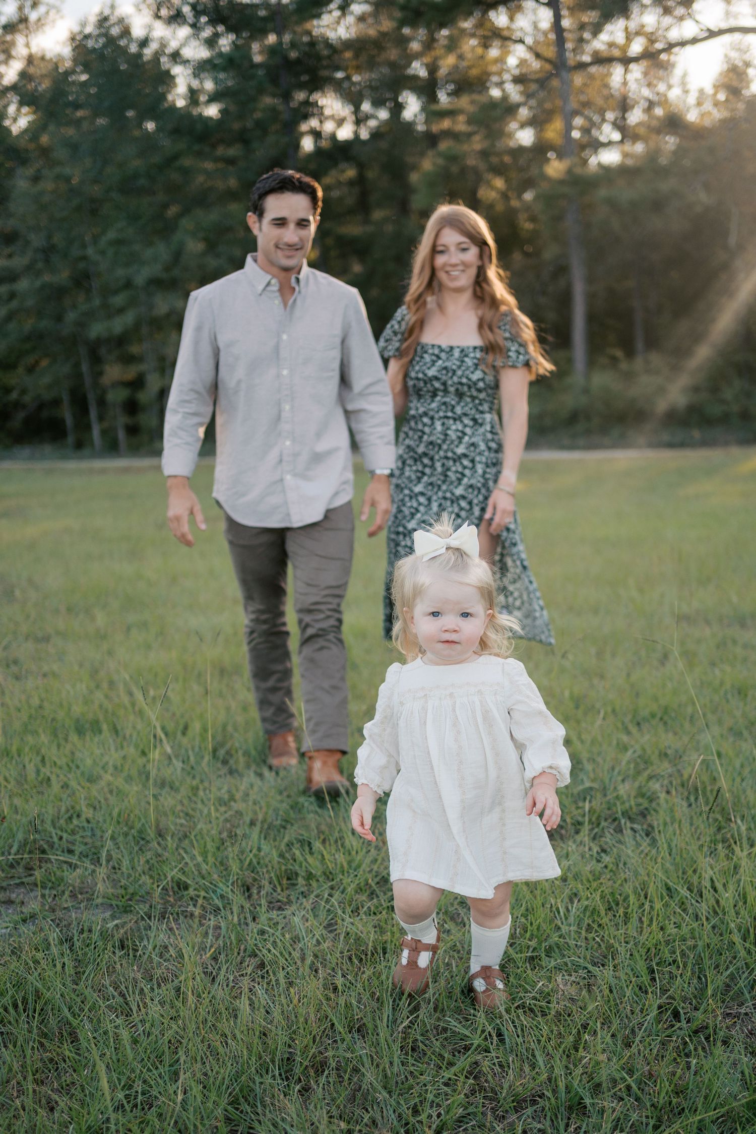 A family walks together through a sunlit grassy field during a summer evening photoshoot.