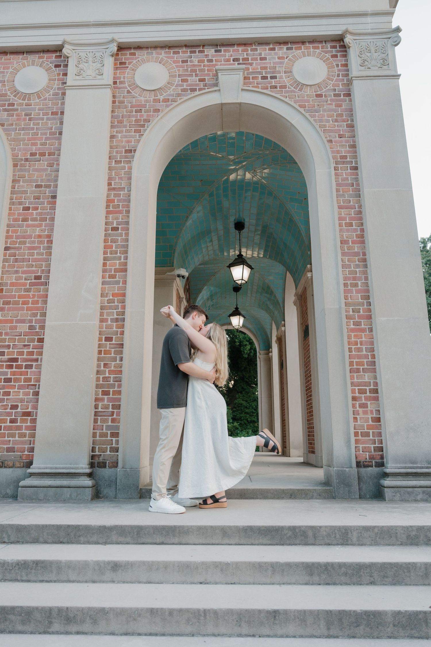 A romantic couple in elegant attire dance and embrace under ornate brick archways during a photo session.