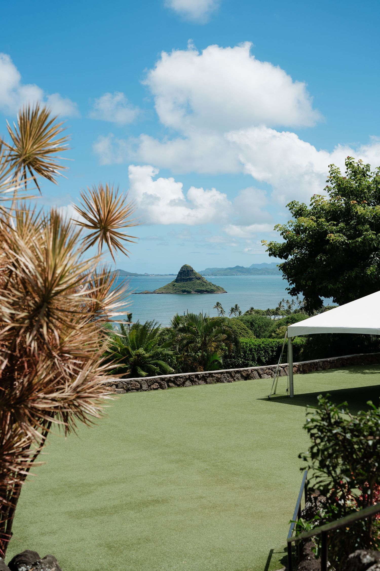Lush green lawn with tropical plants overlooking Chinaman's Hat island in Kaneohe Bay, Hawaii under blue skies.
