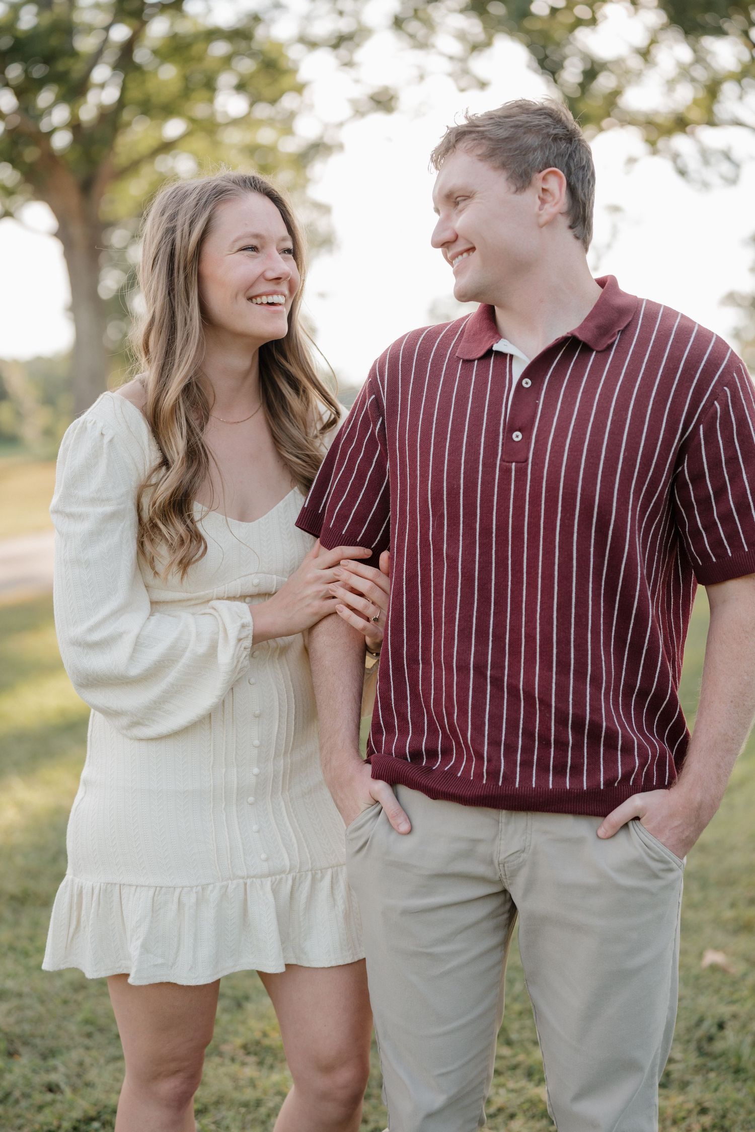 A couple shares joyful moments together outdoors wearing burgundy striped and white outfits in warm sunlight.