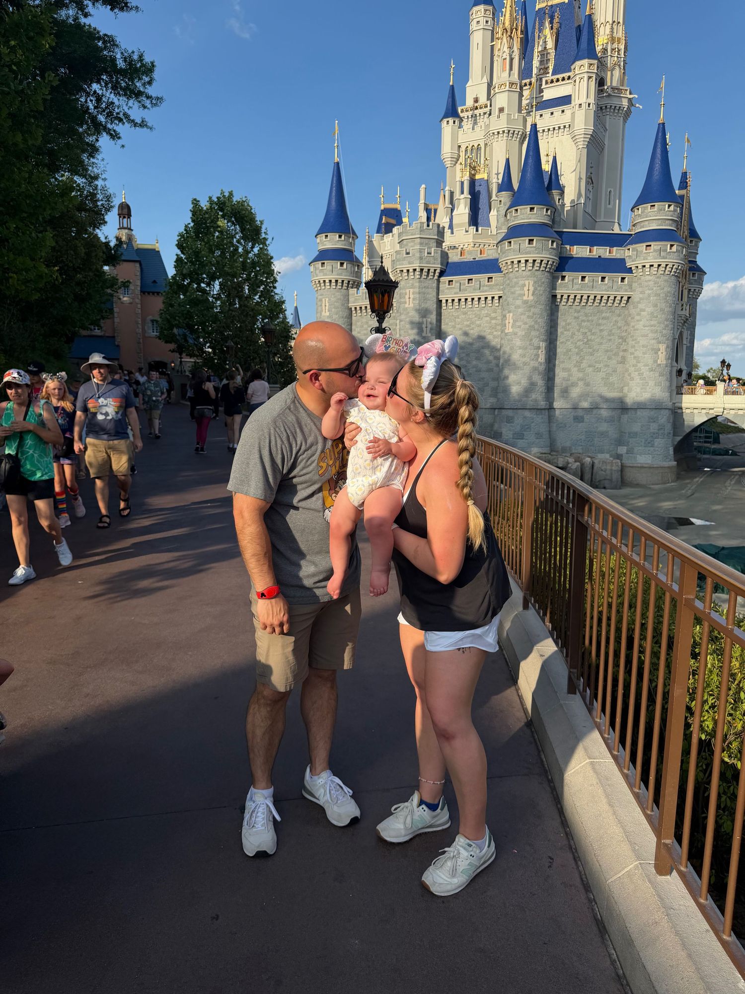 Family with baby kissing at Magic Kingdom, Cinderella Castle backdrop, Walt Disney World, sunny day.